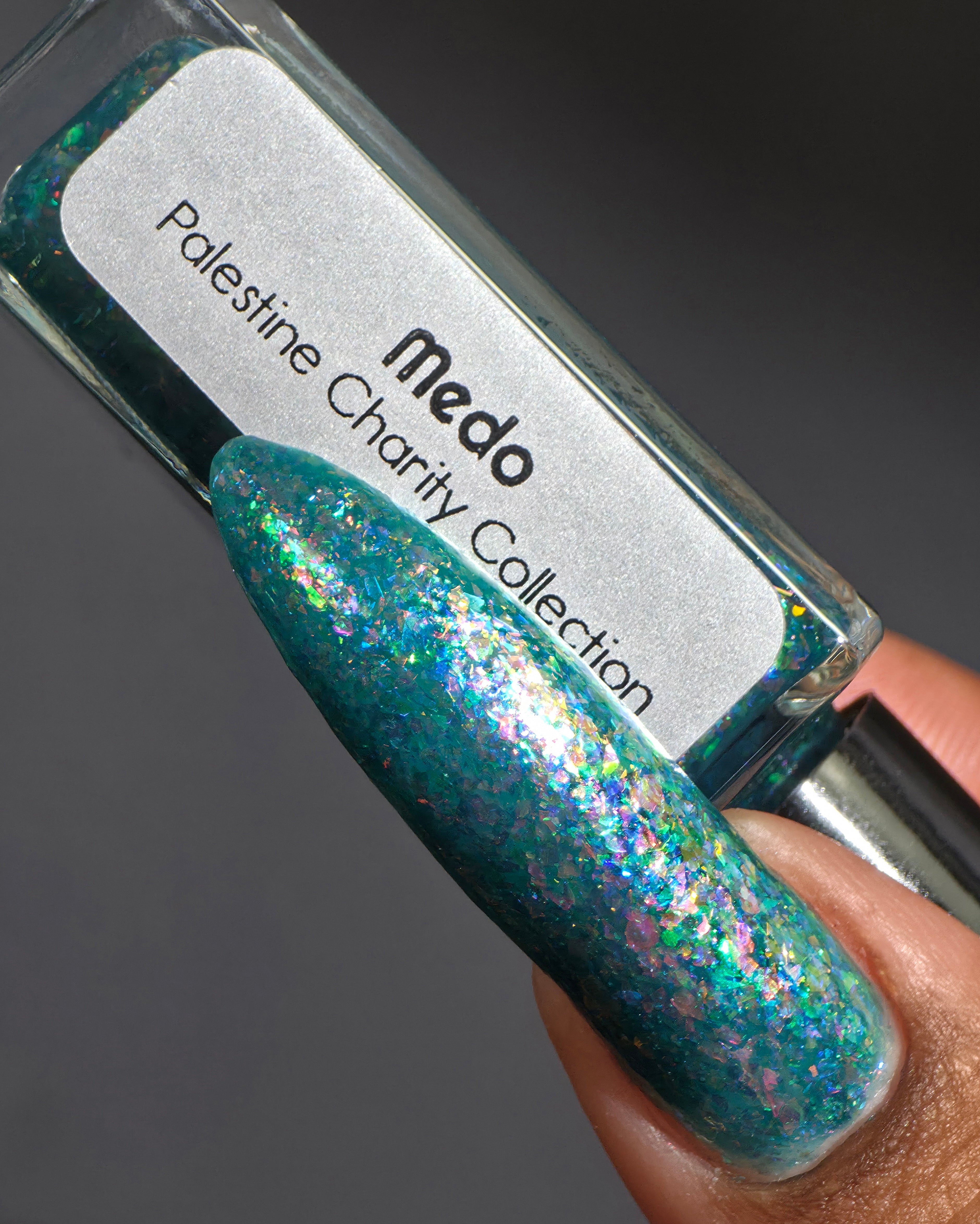 Medo by Glitch Lacquer, teal jelly with iridescent flakies bottle and swatch on medium-deep skin