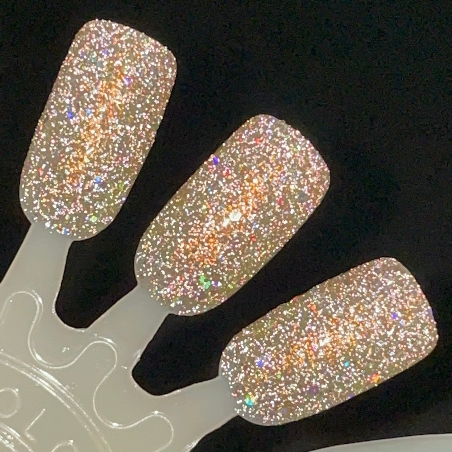 Sunny Side Up by Dam Nail Polish, champagne-gold base with silver holographic and reflective glitter blazing under direct flash, swatch stick