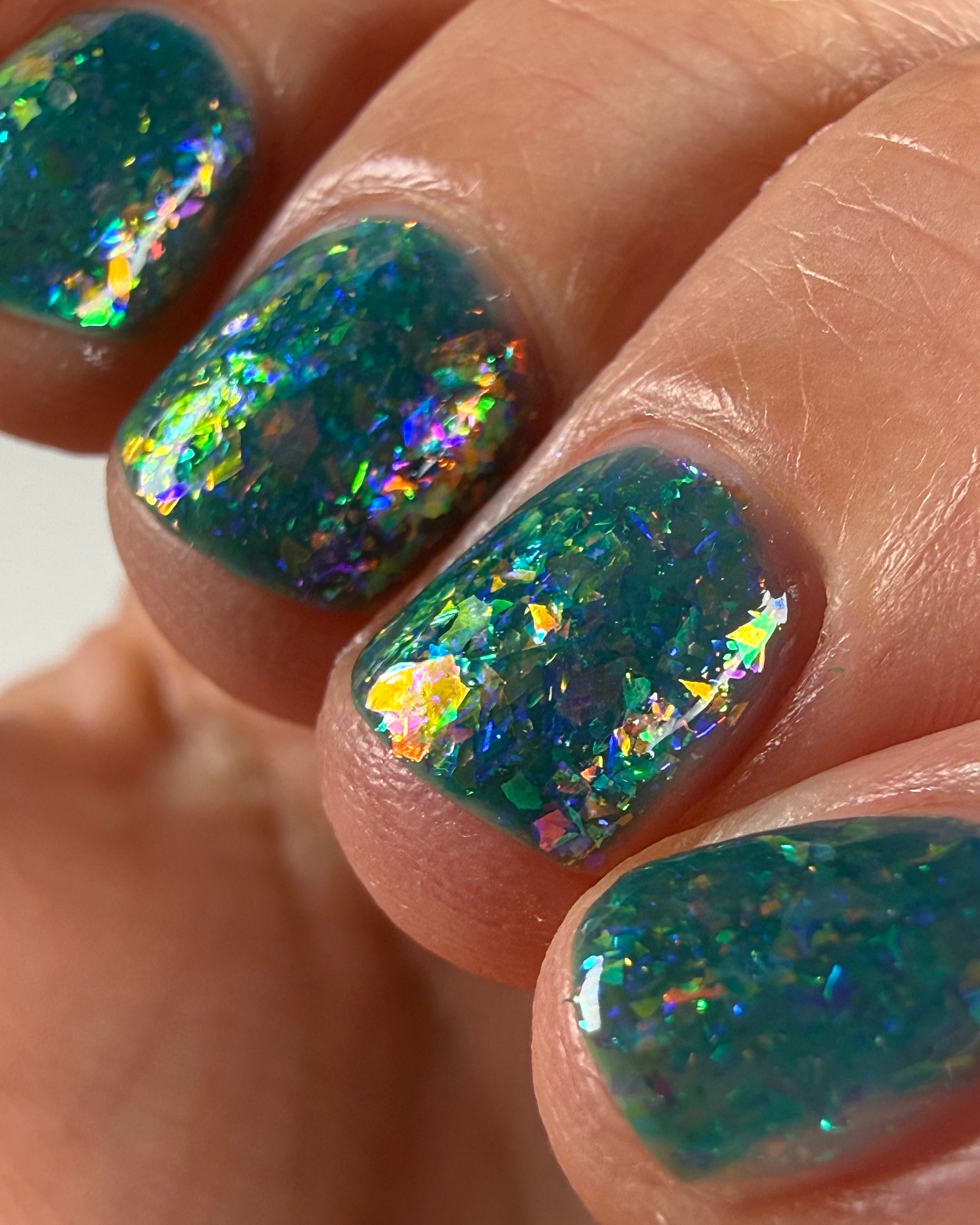 Medo by Glitch Lacquer, macro close-up of teal jelly with iridescent rainbow flakies on light skin