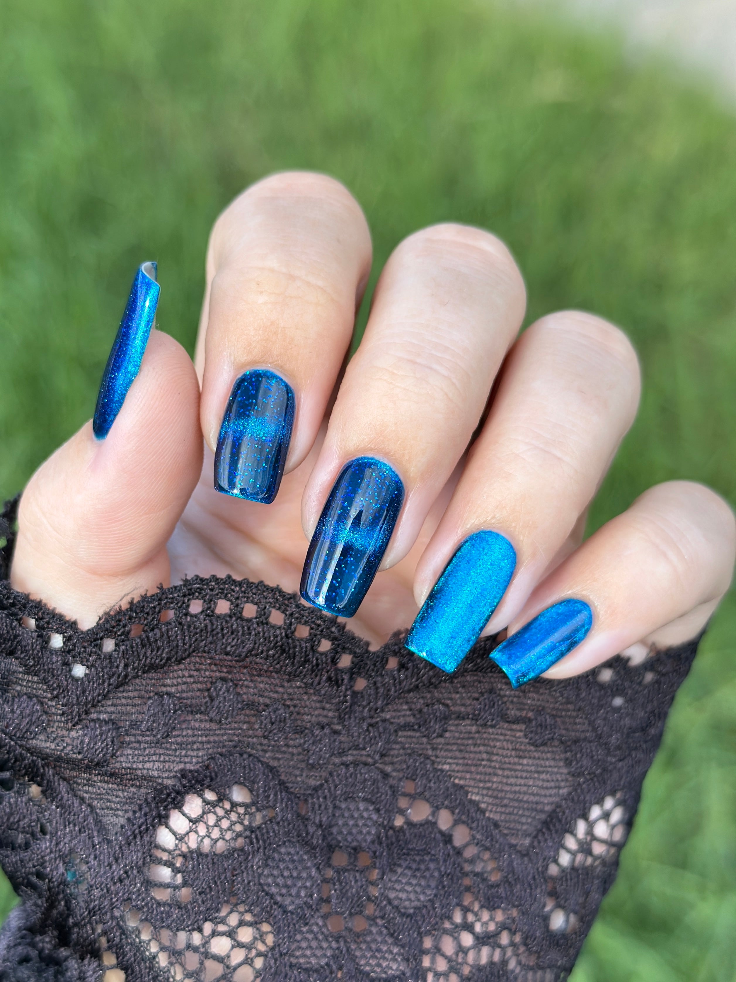 Heart of the Ocean by Glitch Lacquer on five nails comparing magnetic stripes against fully glittered finishes, deep blue jelly with blue glitters, light-medium skin tone, bright daylight.