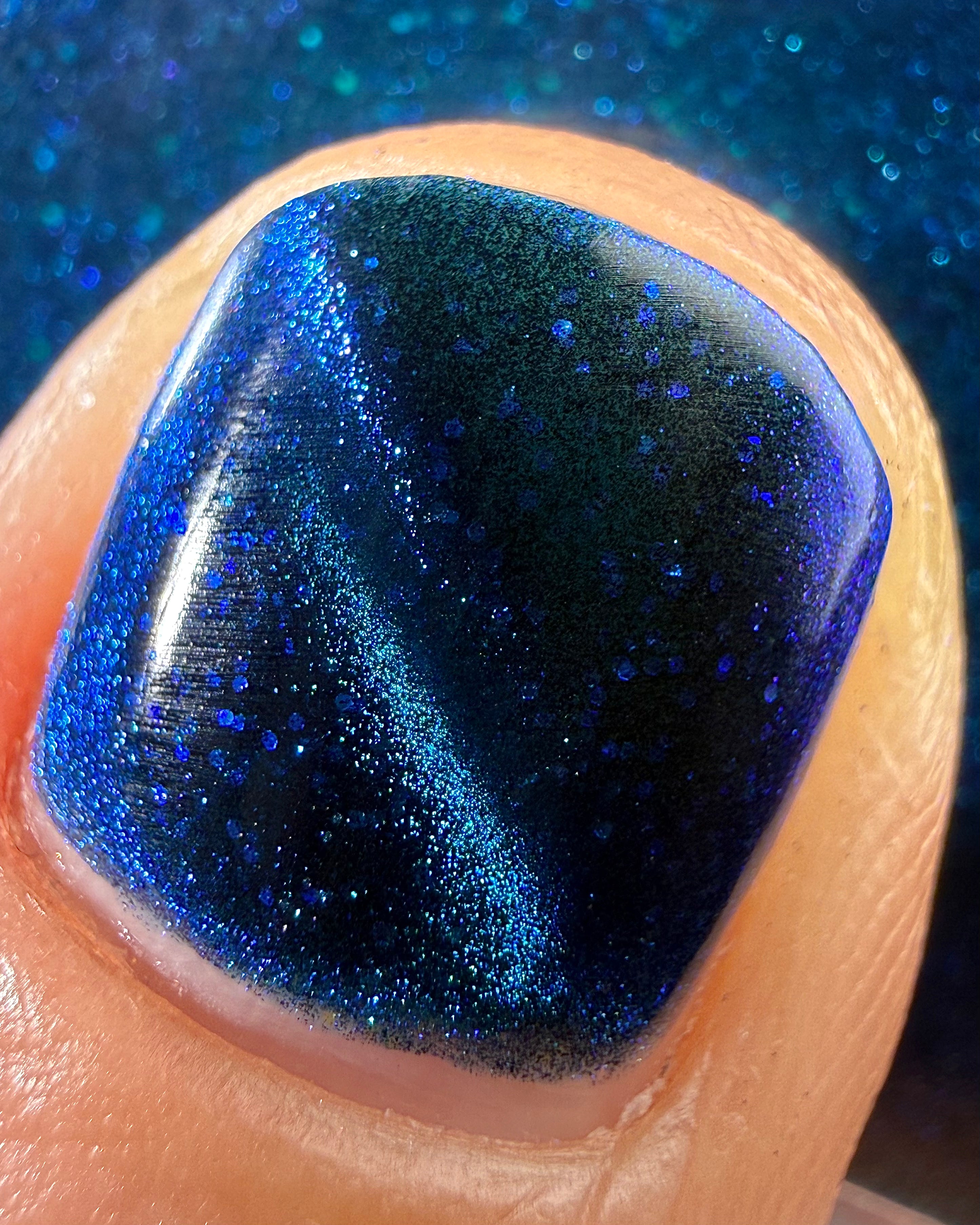 Heart of the Ocean by Glitch Lacquer macro detail on a single nail, deep blue magnetic jelly with blue-to-purple shimmer and blue glitters, light-medium skin tone, studio lighting.