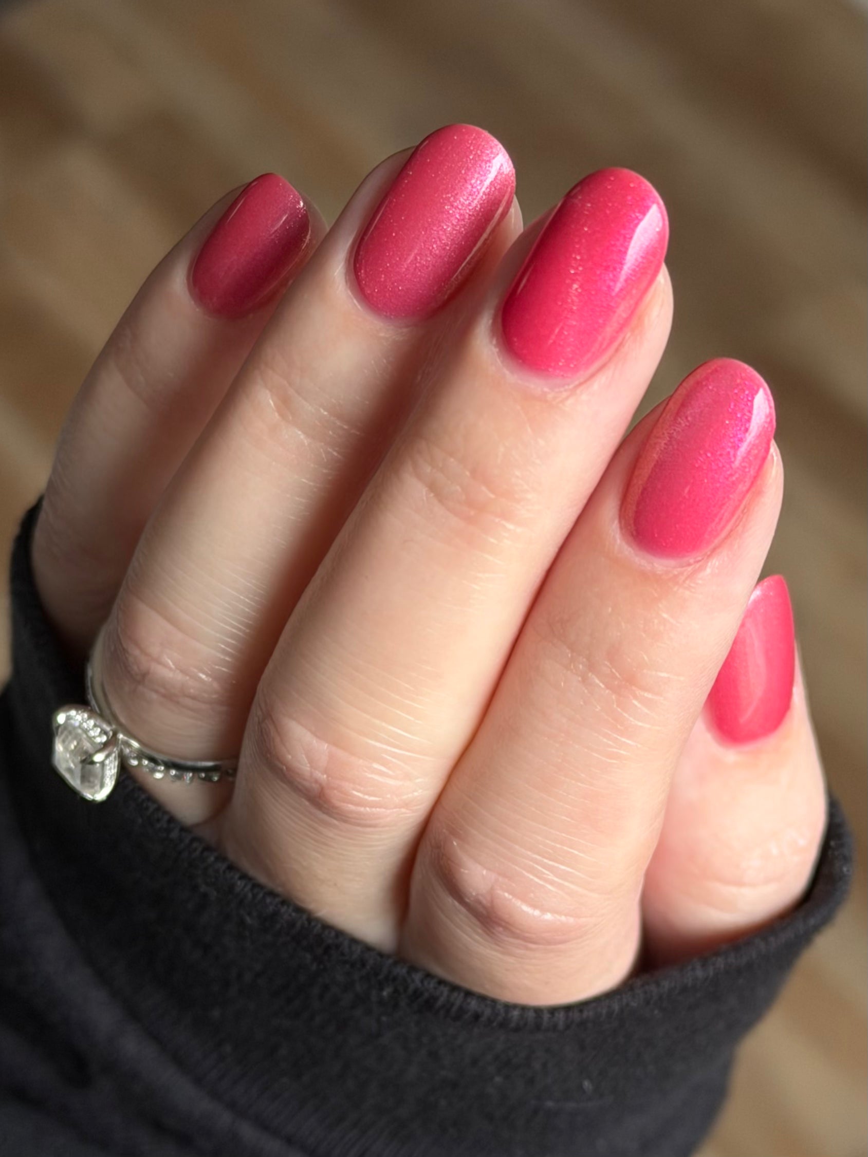 Lovey Dovey by Glitch Lacquer on five oval nails worn with a square-cut diamond ring, warm pink polish with pink-to-gold reflective shimmer and silver magnetic pigment, light skin tone, bright daylight.