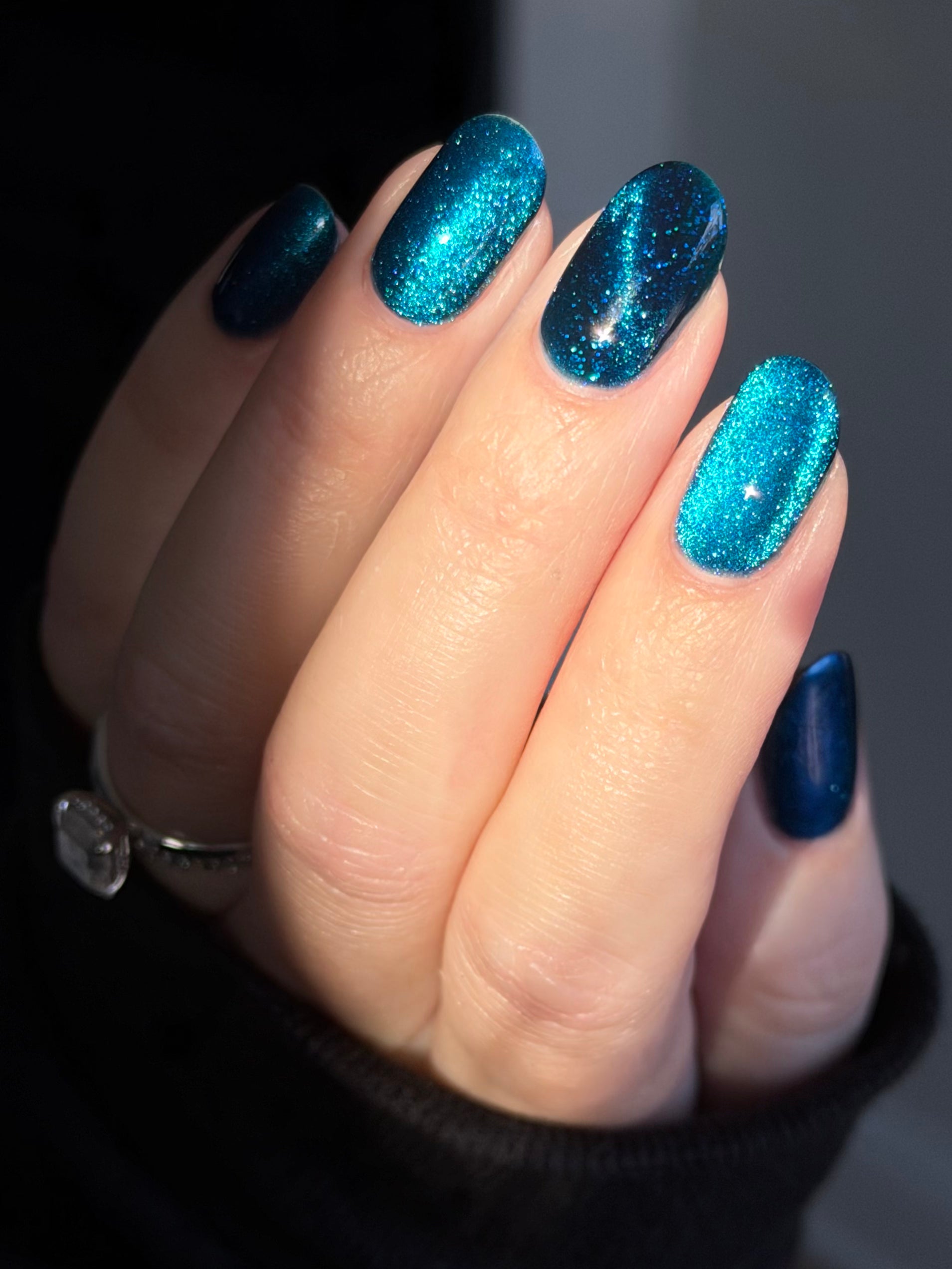 Heart of the Ocean by Glitch Lacquer on five oval nails, deep blue magnetic jelly with blue-to-purple shift and blue glitters, light skin tone, bright studio lighting.