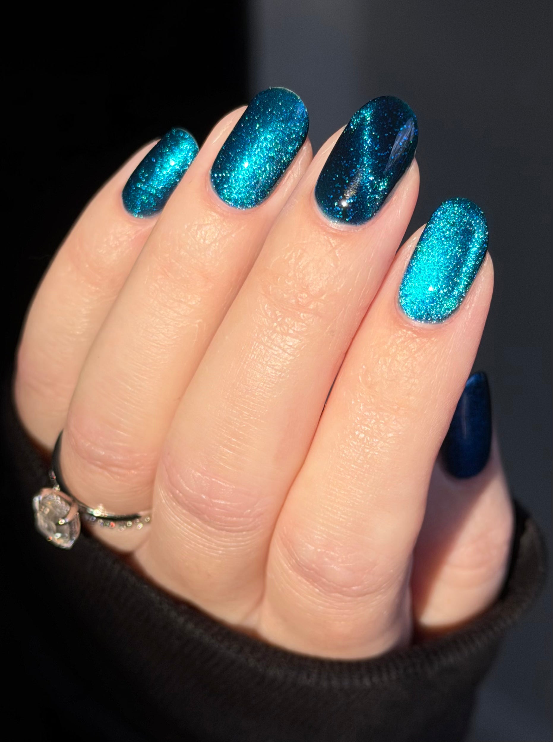 Heart of the Ocean by Glitch Lacquer on five oval nails, deep blue magnetic jelly with blue glitters, light skin tone, bright daylight.