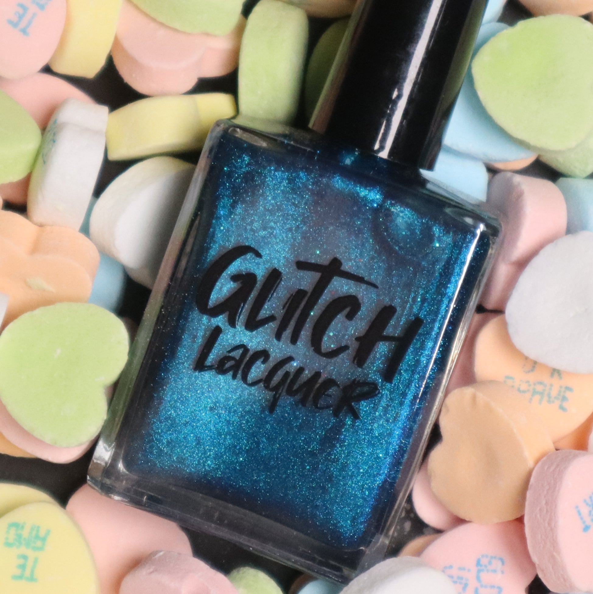 Heart of the Ocean by Glitch Lacquer bottle front shown among pastel heart-shaped candies, deep blue magnetic jelly with blue glitters, studio lighting.