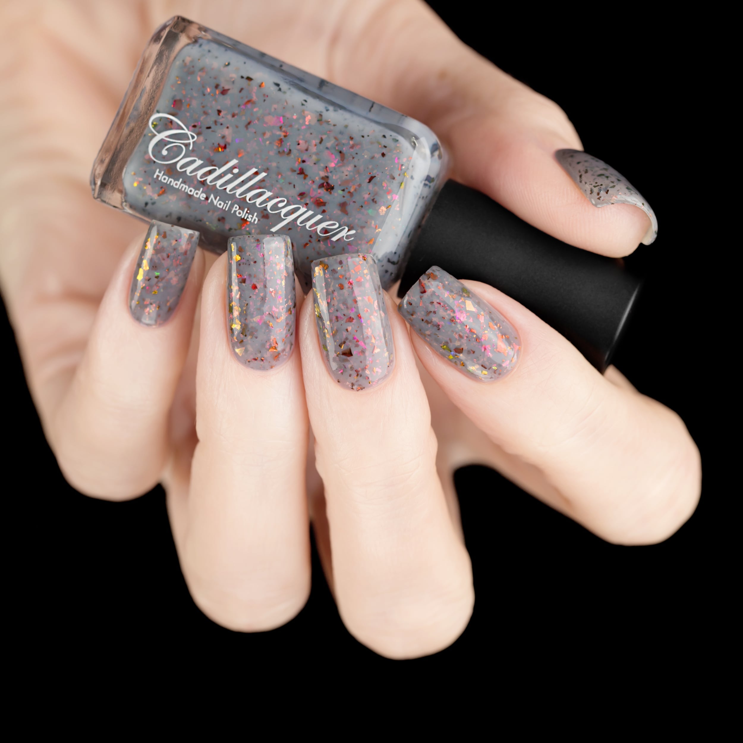 Cadillacquer Daydreaming grey red chameleon iridescent crelly nail polish, bottle held with five-nail swatch, light skin, studio lighting
