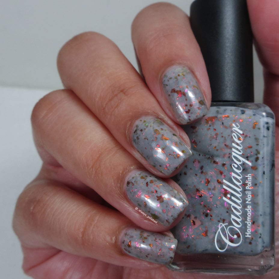 Cadillacquer Daydreaming grey red chameleon iridescent crelly nail polish, bottle held with four-nail swatch, light skin, indoor warm lighting