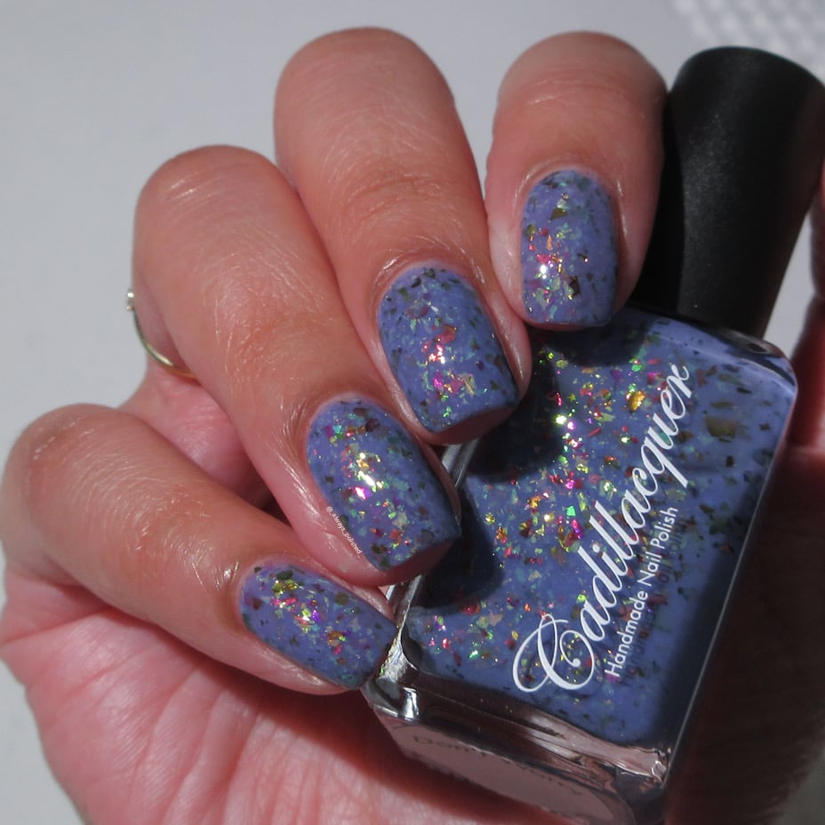 Cadillacquer Don't Worry purple pink chameleon iridescent crelly nail polish, bottle held with four-nail swatch, light skin, bright daylight lighting