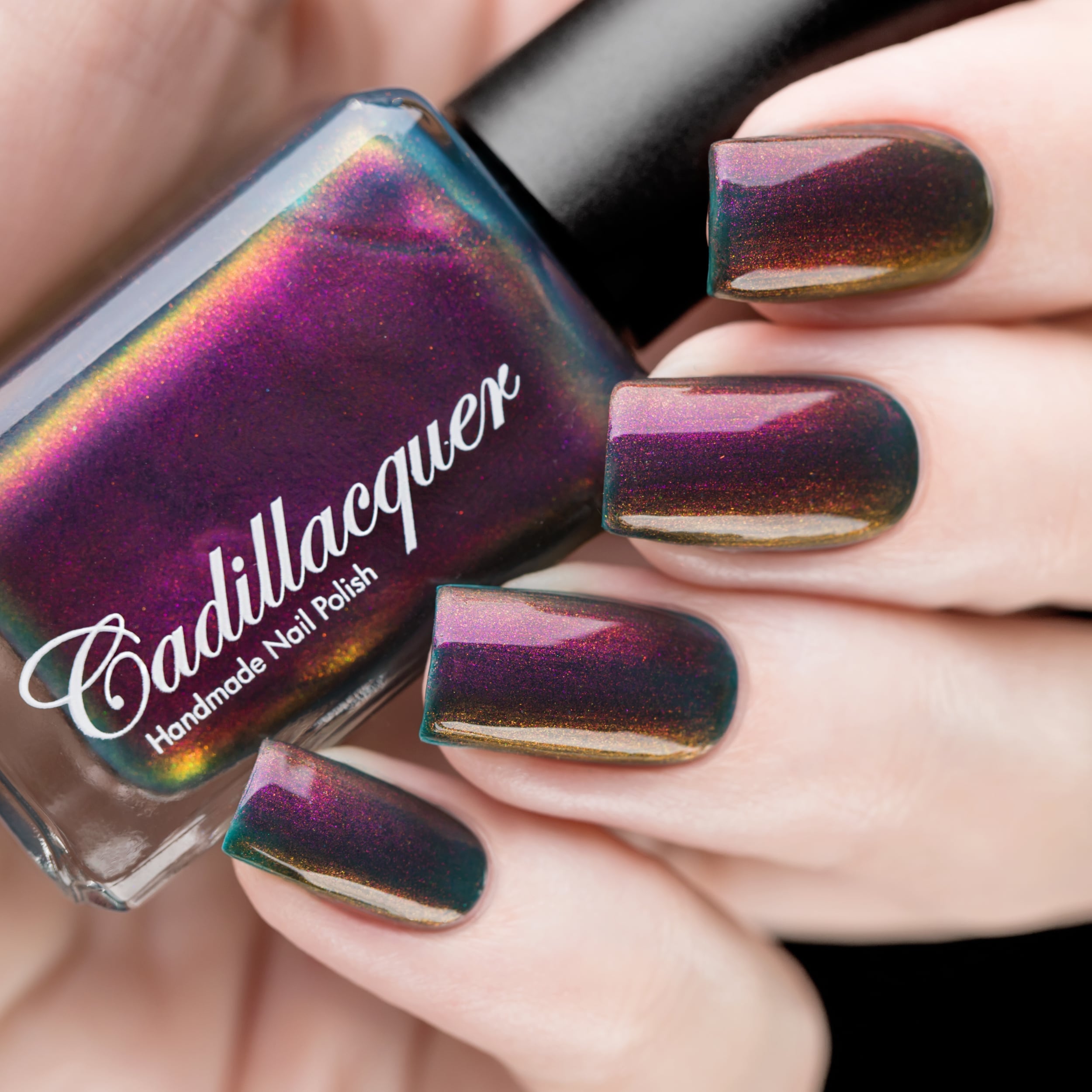 Multichrome shimmer Cadillacquer nail polish in Fear What You Will Become, shown in bottle held in hand alongside five swatched squoval nails, shifting from dark murky teal through deep magenta-plum to bronze-amber and orange depending on angle, packed with red-orange and magenta shimmer flash, on light skin tone, studio lighting, swatched by @rafinails
