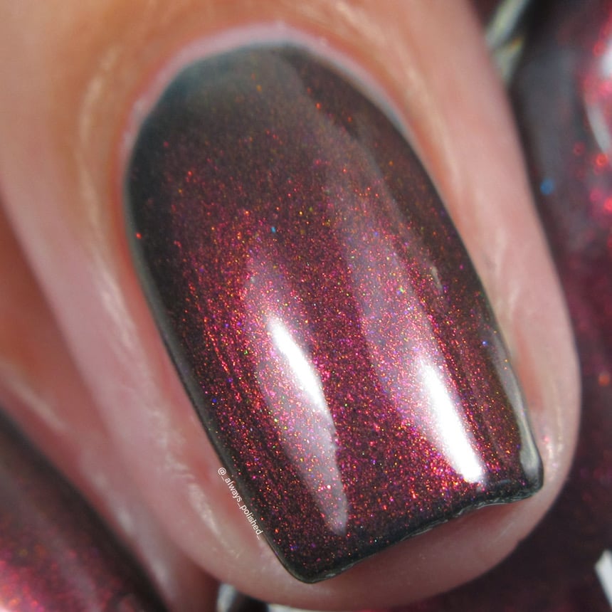 Holographic shimmer Cadillacquer nail polish in Fear What You Will Become, macro swatch on a single short natural nail showing a very dark blackened base densely packed with magenta-to-orange linear holographic shimmer and rare teal and blue sparks, light-medium skin tone, indoor warm lighting, swatched by @_always_polished_