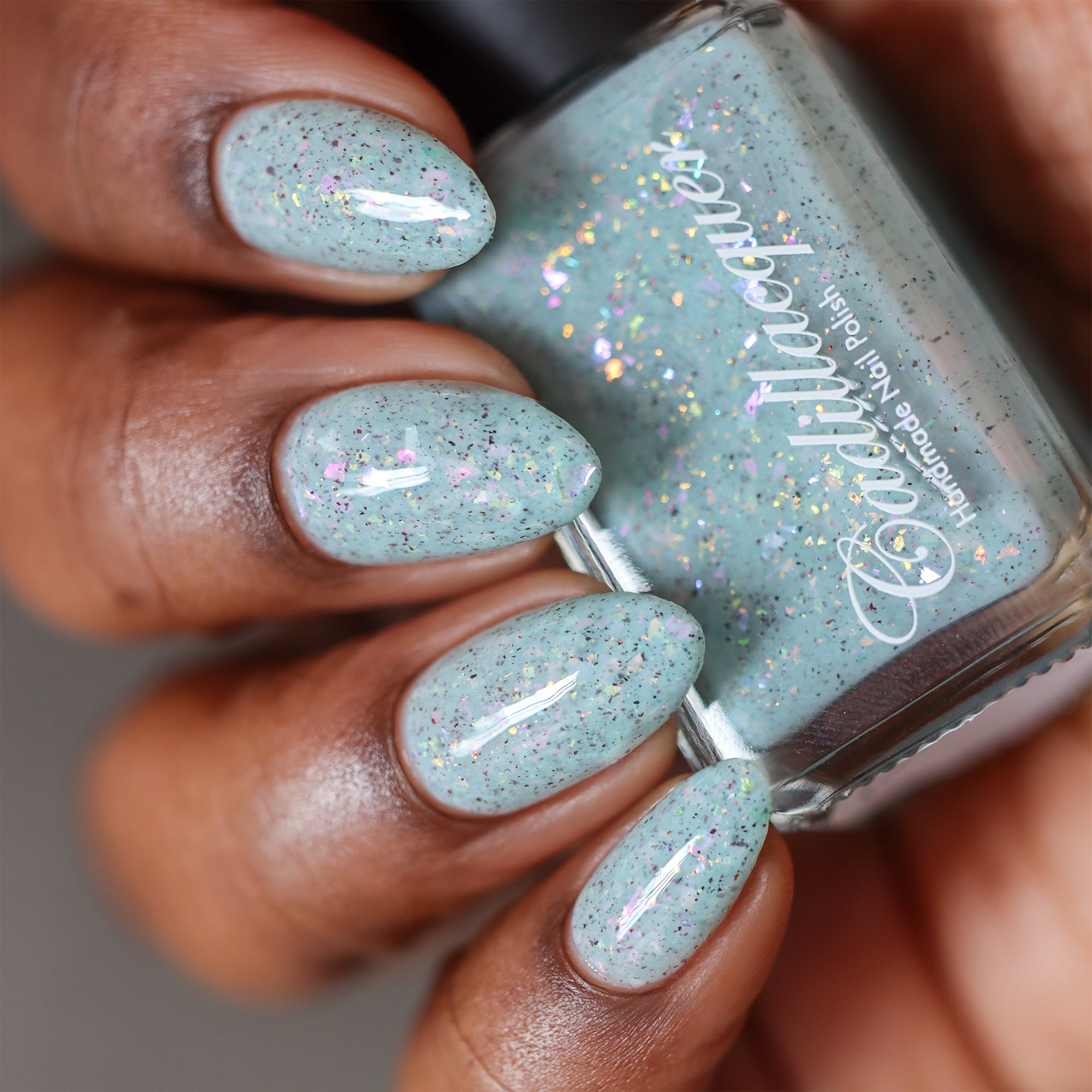 Cadillacquer Fresh Sheets pastel mint iridescent crelly nail polish, bottle held with four-nail swatch, rich skin, studio lighting