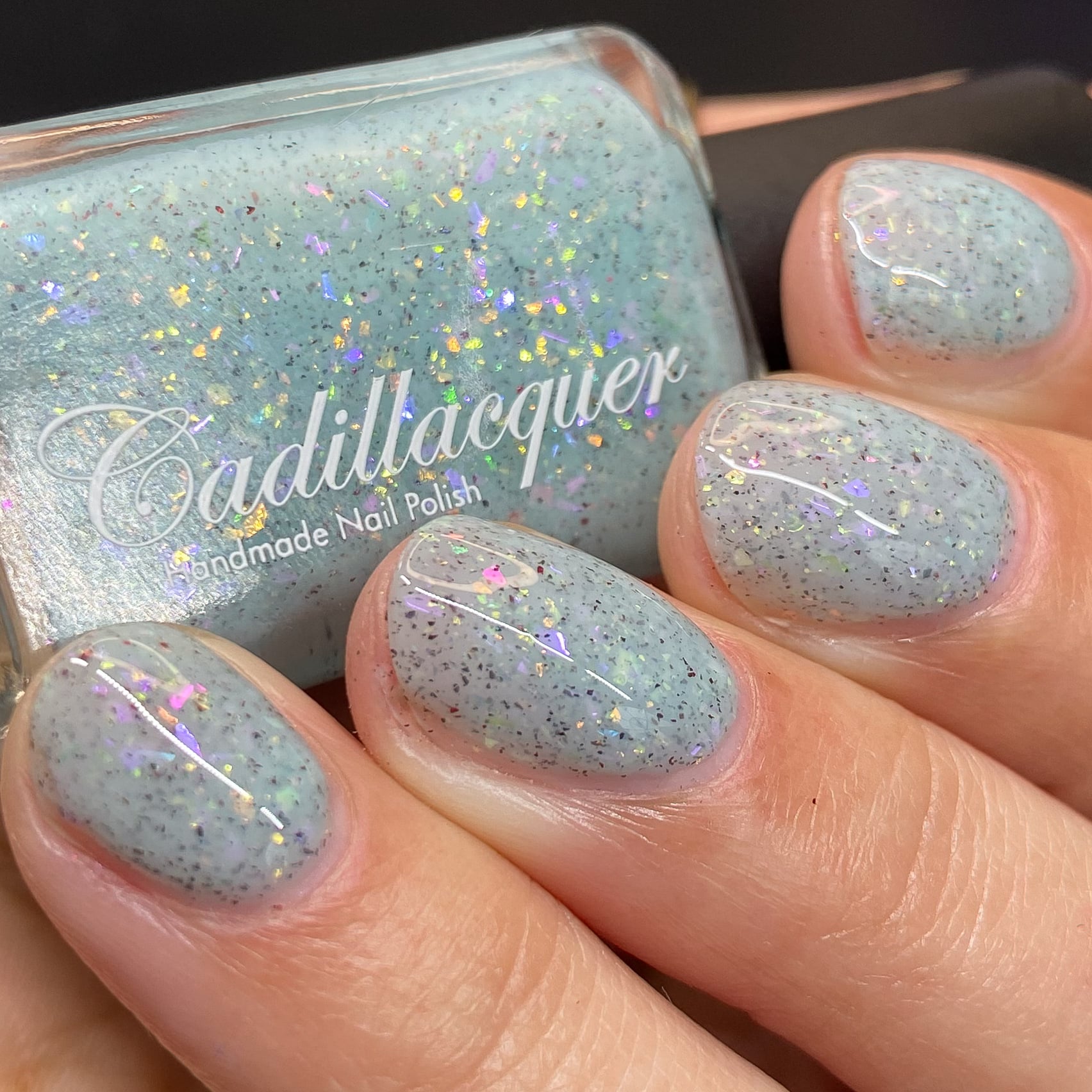 Cadillacquer Fresh Sheets pastel mint iridescent crelly nail polish, bottle held with four-nail swatch, light skin, studio lighting