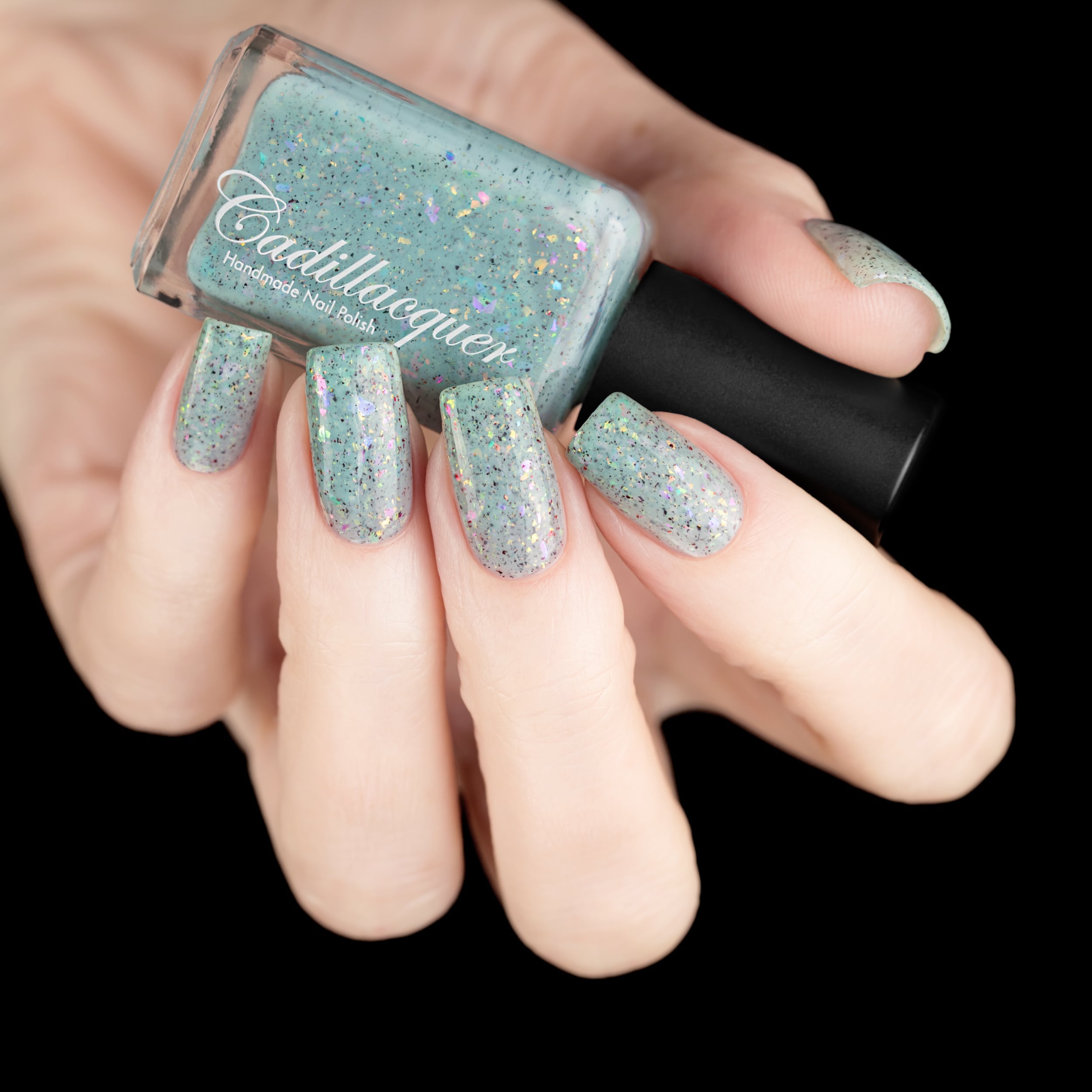 Cadillacquer Fresh Sheets pastel mint iridescent crelly nail polish, bottle held with five-nail swatch, light skin, studio lighting