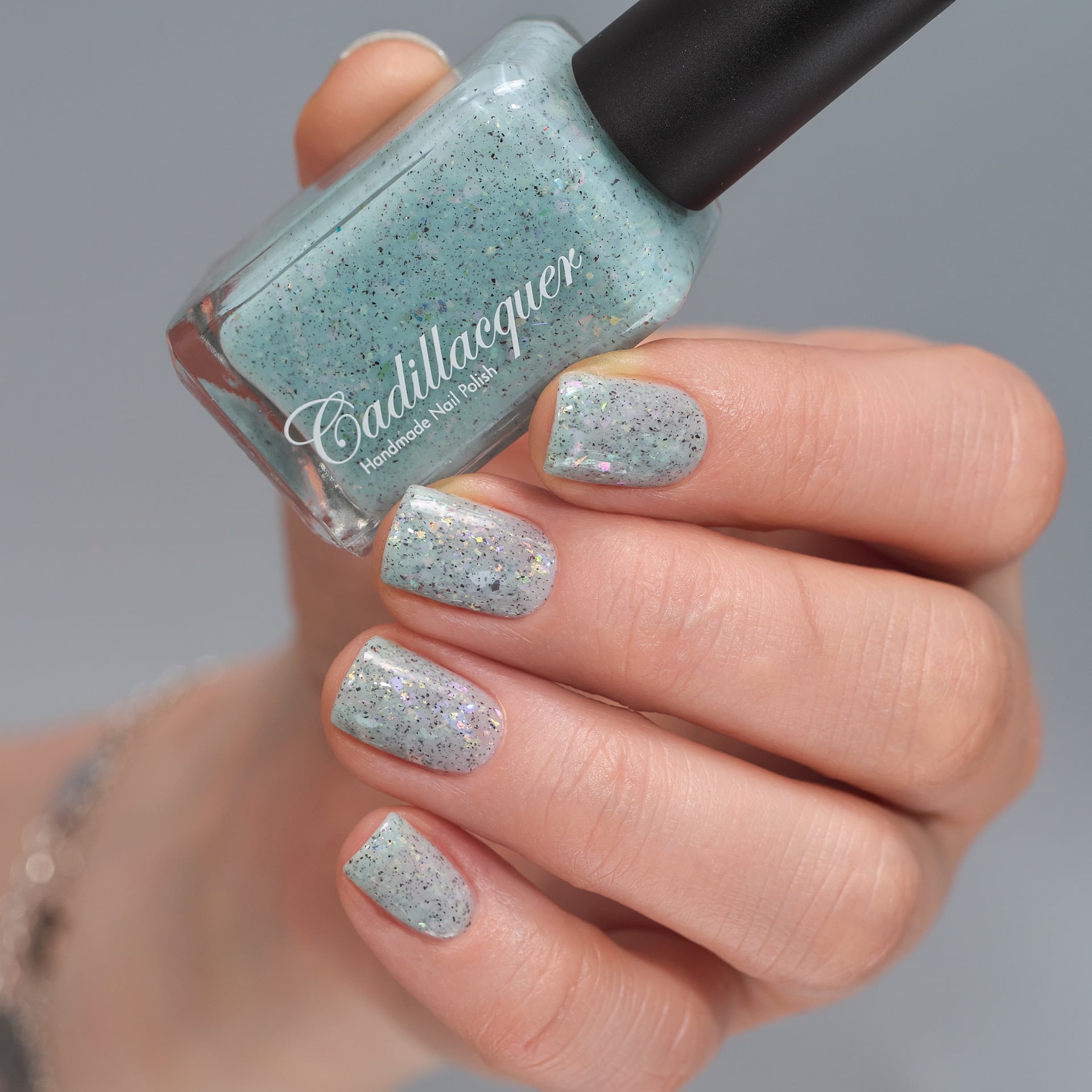 Cadillacquer Fresh Sheets pastel mint iridescent crelly nail polish, bottle held with four-nail swatch, light skin, studio lighting