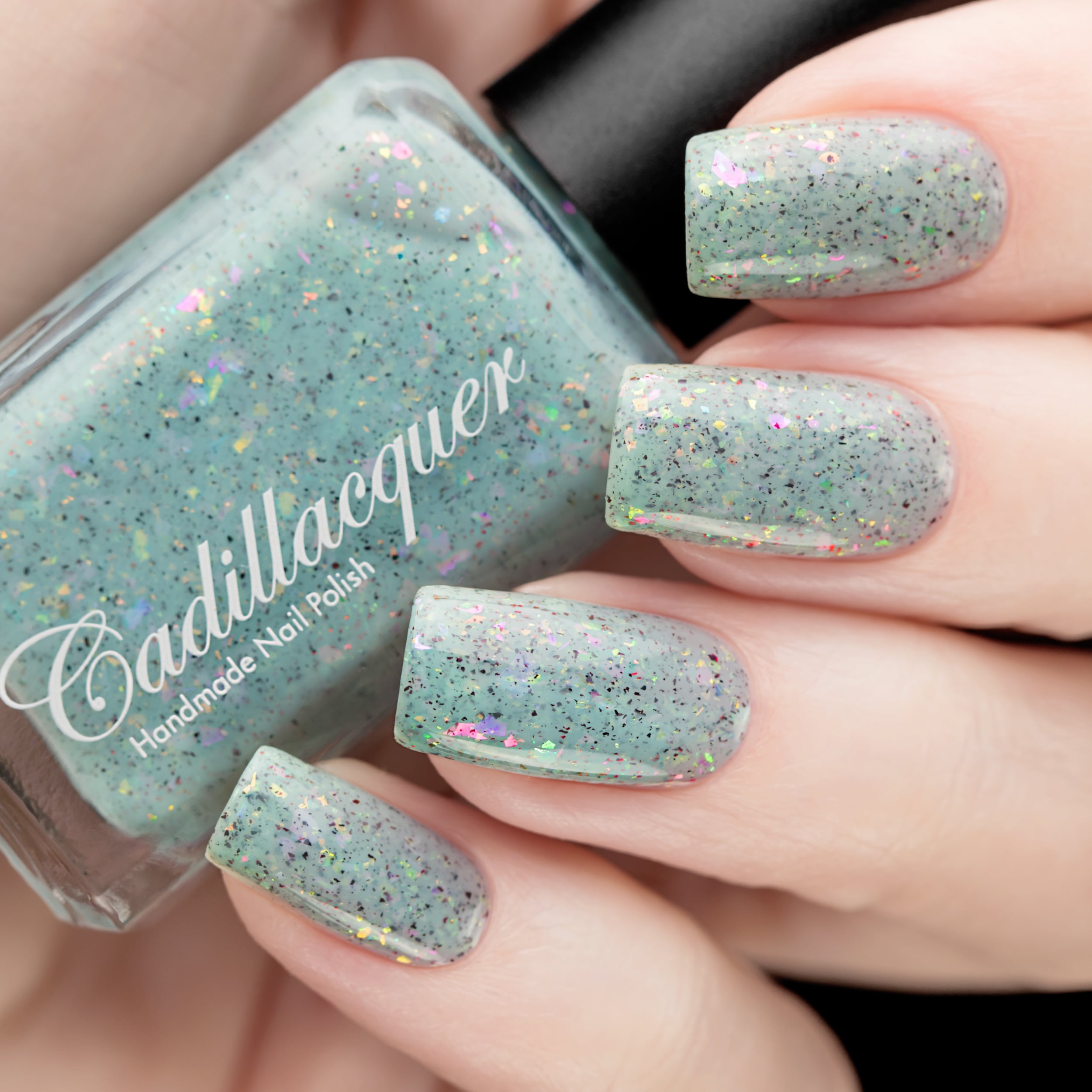 Cadillacquer Fresh Sheets pastel mint iridescent crelly nail polish, bottle held with four-nail swatch, light skin, studio lighting