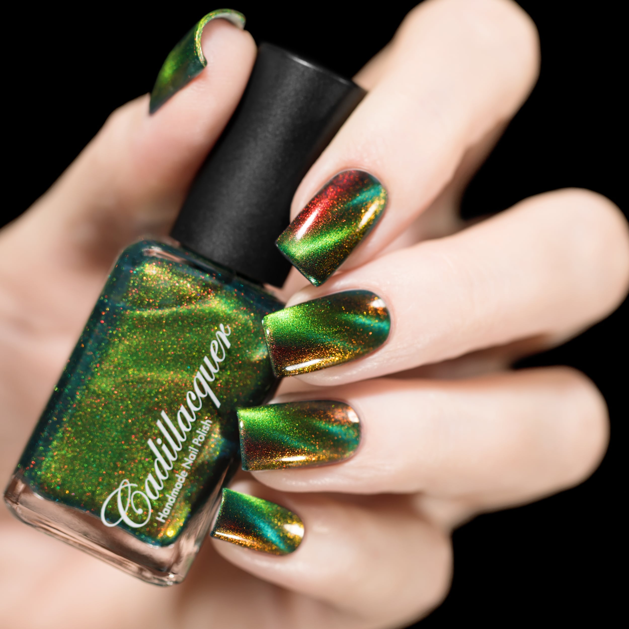 Magnetic multichrome holographic Cadillacquer nail polish in I Found A Place, shown in bottle held in hand with five swatched nails displaying lime green magnetic band over deep forest green field with vivid red-to-orange aurora shimmer, light skin tone, studio lighting, swatched by @rafinails