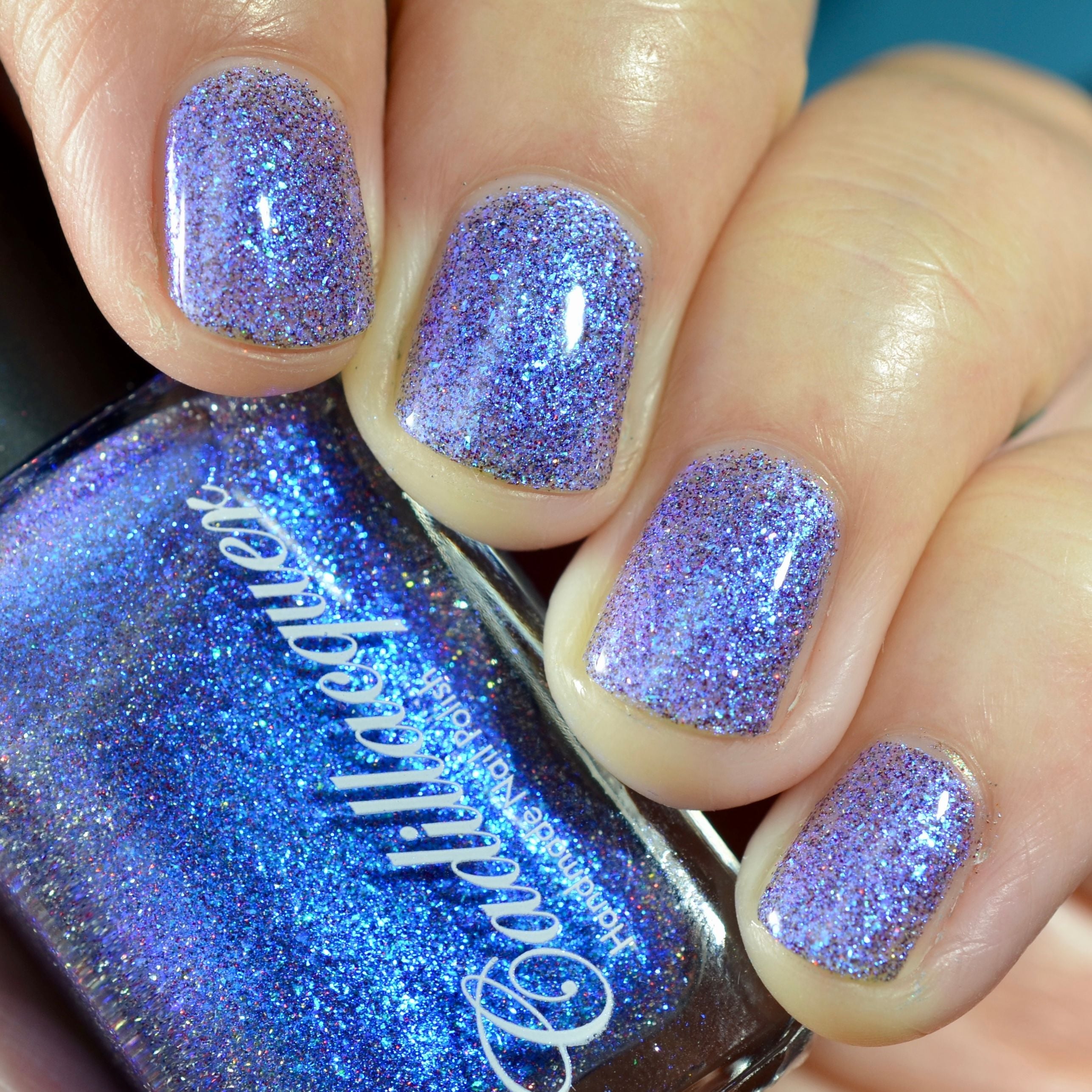 Shimmer, micro flake and holographic glitter Cadillacquer nail polish in I'll Be Right Back, shown as a bottle-and-nails swatch with five square nails reading sheer lavender-violet packed with blue iridescent micro flakes and sparkling holographic glitter, while the bottle reads vivid electric blue, on light skin tone under studio lighting, swatched by @caitlinswatches