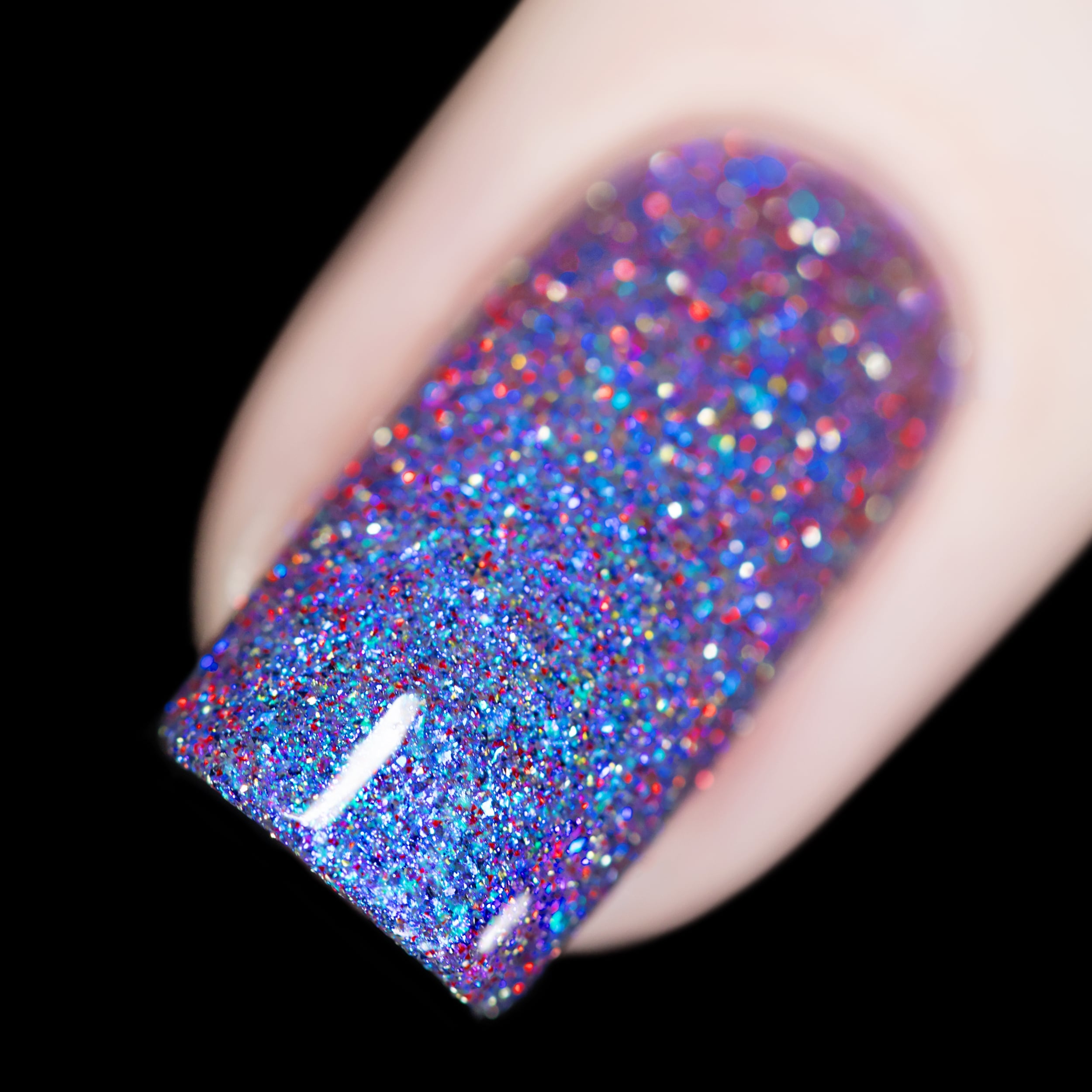 Holographic glitter and shimmer Cadillacquer nail polish in I'll Be Right Back, shown as a macro swatch on a single square nail packed with blue micro flakes, vivid red and charcoal reflective glitter, and icy blue shimmer against a clear base, light skin tone, shot under direct flash on a black background, swatched by @rafinails