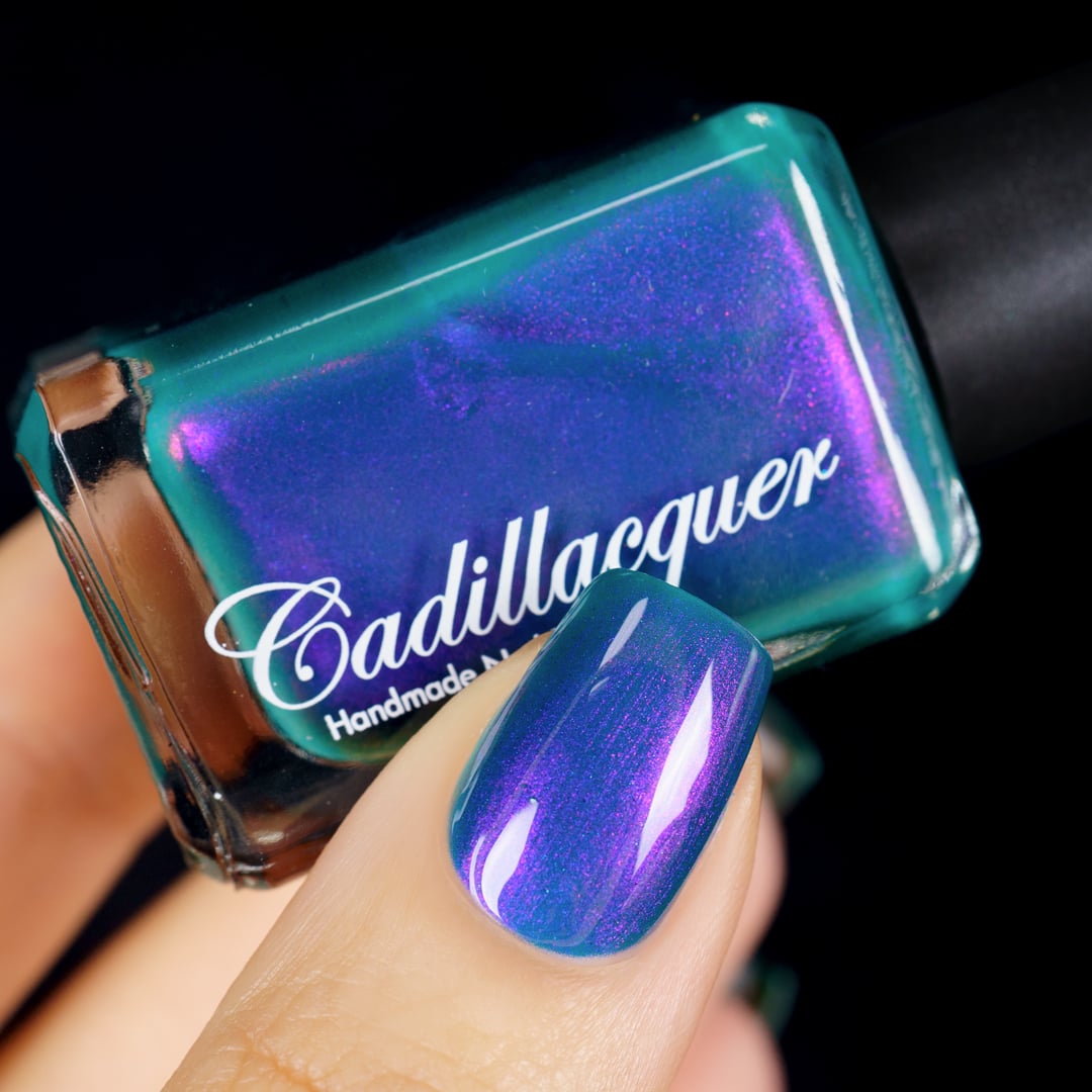 Multichrome shimmer Cadillacquer nail polish in It's All For You, showing one swatched nail alongside the bottle held in hand, the bottle edge reveals a clean teal-green base while the bottle face and nail shift dramatically through violet-purple and magenta-pink shimmer at various angles, light skin tone visible, studio lighting, swatched by @yyulia_m