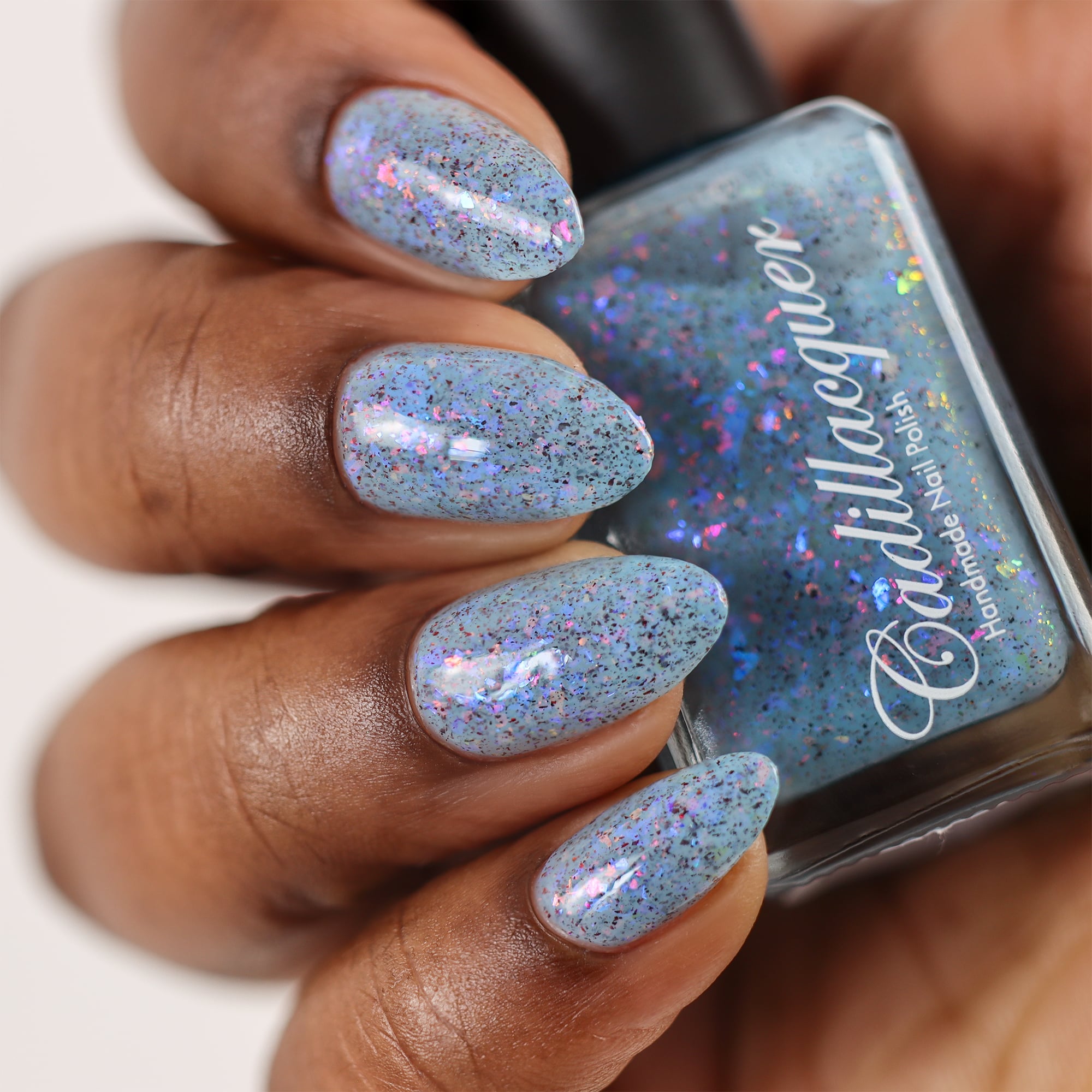 Cadillacquer Just Breathe pastel blue iridescent crelly nail polish, bottle held with four-nail swatch, rich skin, studio lighting
