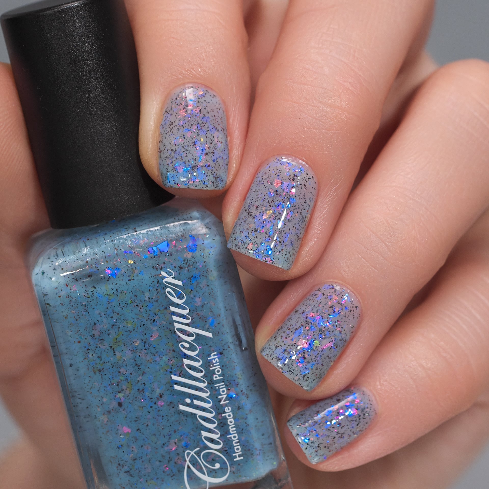 Cadillacquer Just Breathe pastel blue iridescent crelly nail polish, bottle held with four-nail swatch, light skin, studio lighting