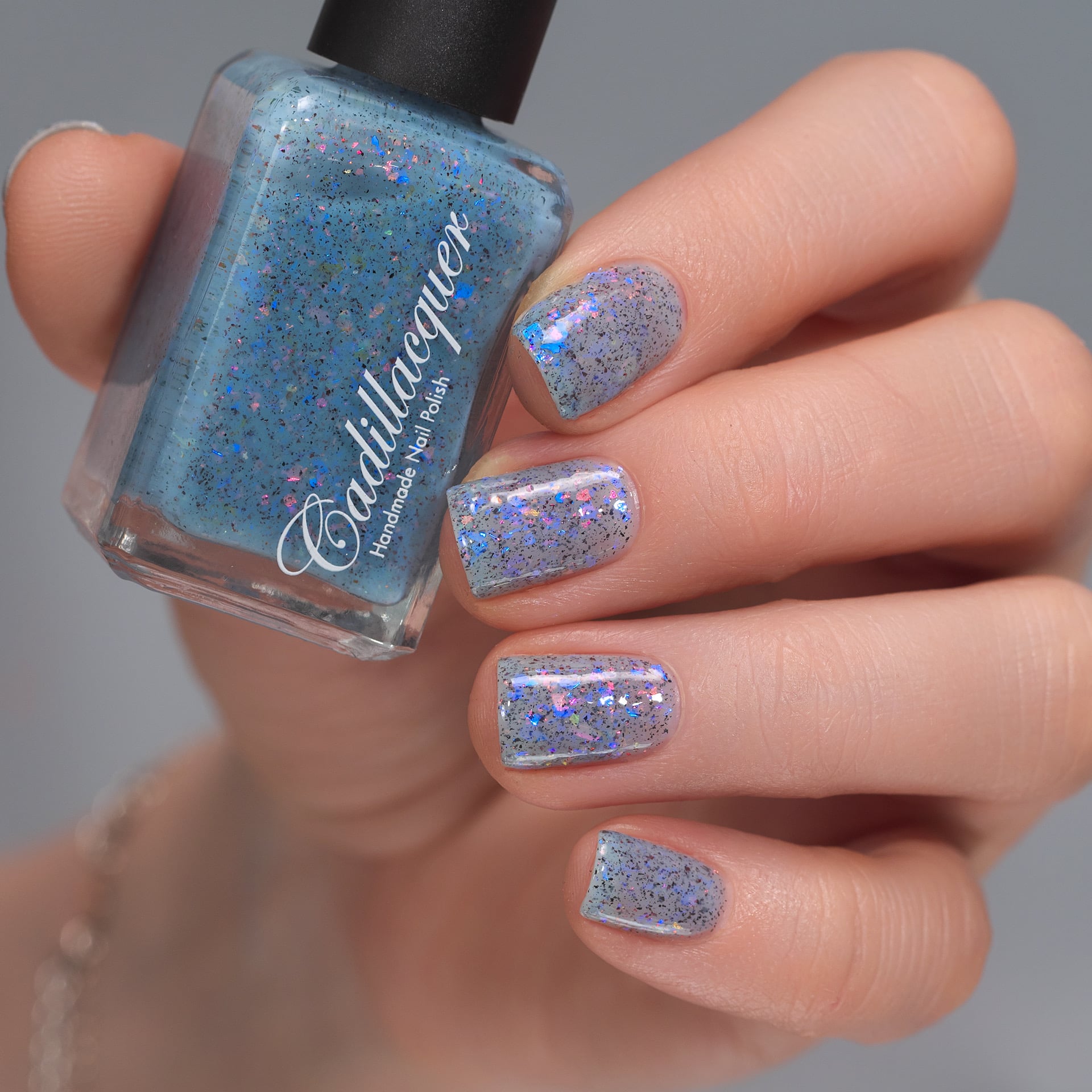 Cadillacquer Just Breathe pastel blue iridescent crelly nail polish, bottle held with four-nail swatch, light skin, studio lighting