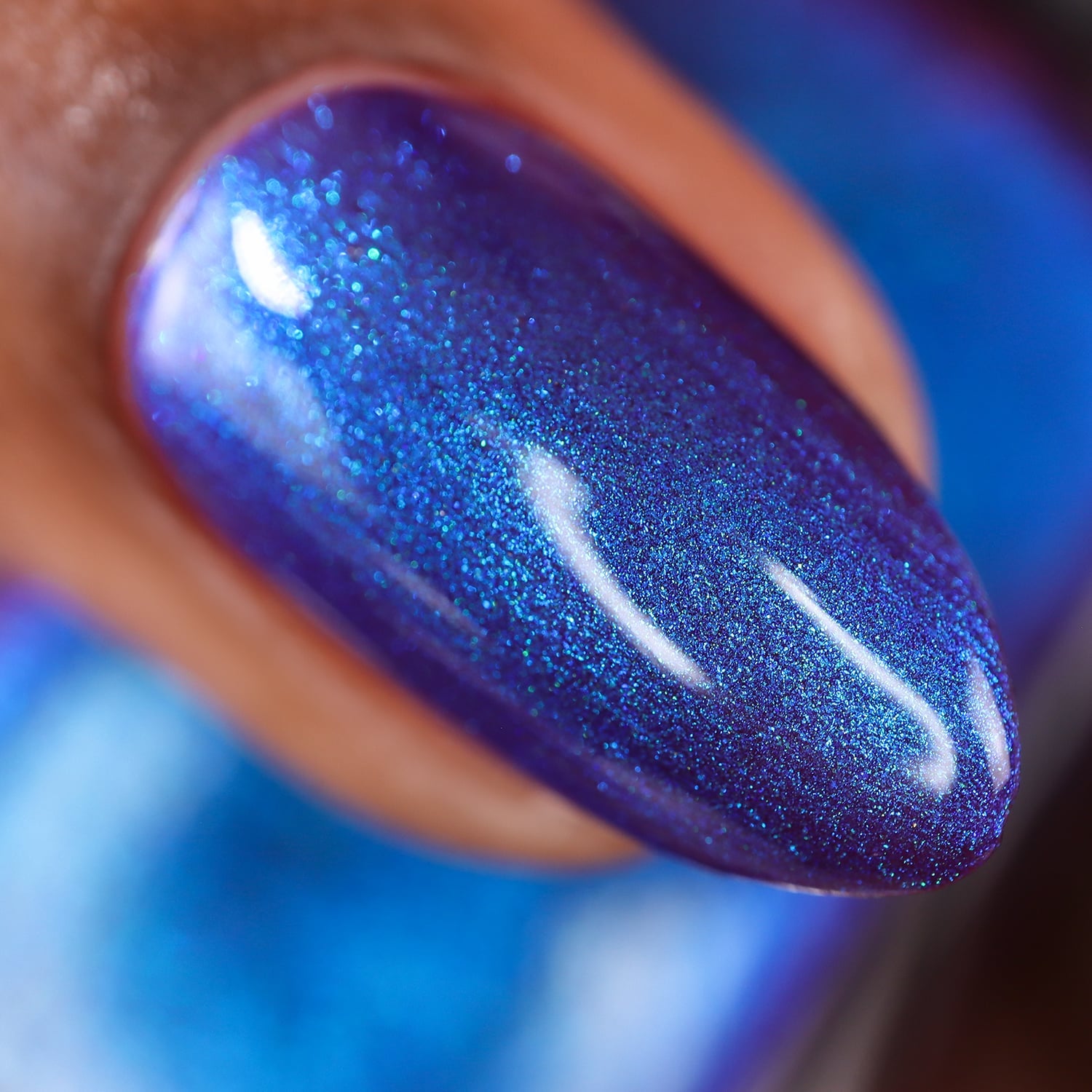 Densely packed blue and teal shimmer Cadillacquer nail polish in Keep Doubting, shown as a macro swatch on a single oval nail on medium skin tone, deep indigo-violet base flooded with vivid electric blue and cyan shimmer particles, studio lighting, swatched by @doseoflolade