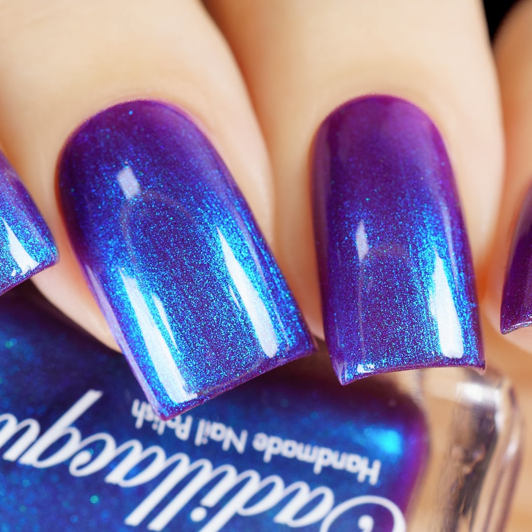 Shimmer Cadillacquer nail polish swatch in Keep Doubting, showing deep violet-mulberry base densely packed with vivid cobalt-blue and cyan shimmer that shifts across the nail surface, worn on five oval nails on light skin tone, shot under studio lighting with a Cadillacquer bottle in the foreground, swatched by @yyulia_m