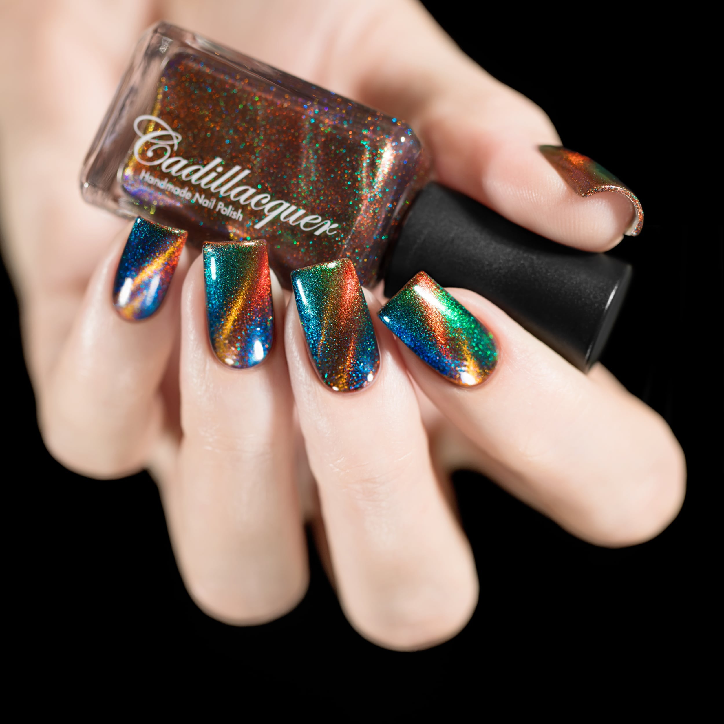 Magnetic holographic multichrome Cadillacquer nail polish in Once You See It, shown in bottle held in hand with five swatched square nails displaying dramatic diagonal copper-orange magnetic band over deep teal-blue field with vivid green and blue aurora shimmer, light skin tone, studio lighting, swatched by @rafinails