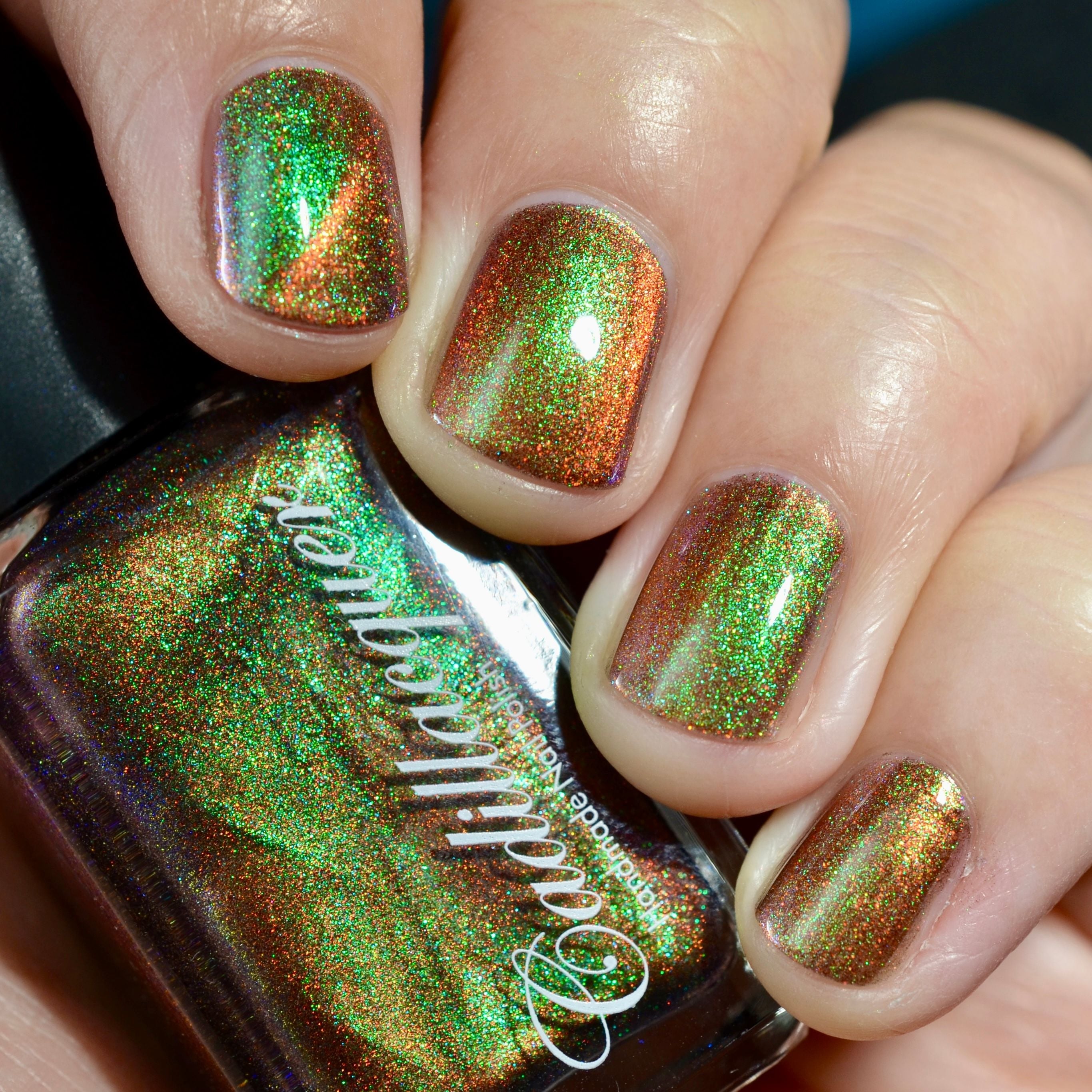 Magnetic holographic multichrome Cadillacquer nail polish in Once You See It, shown as swatch on four short natural nails with a bottle held in hand, displaying a deep red-brown base with vivid green aurora shimmer flash and orange-copper magnetic band, on light skin tone, studio lighting, swatched by @caitlinswatches