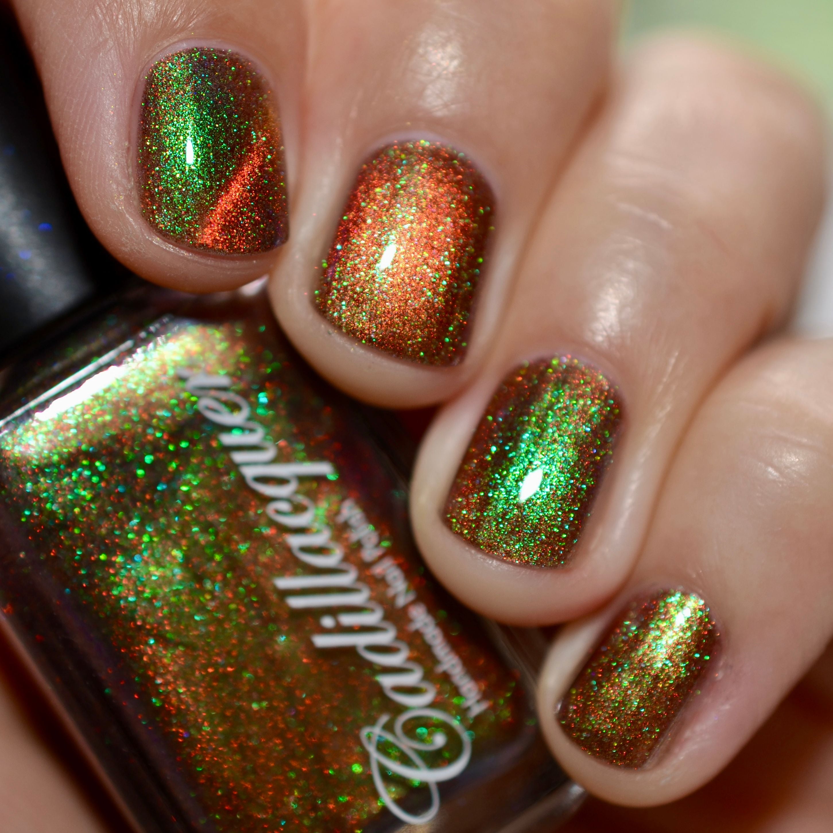 Holographic magnetic multichrome Cadillacquer nail polish in Once You See It, shown on five short natural nails and held bottle, with a deep red-brown carrier base, vivid copper-orange magnetic band, and intense green-to-teal aurora shimmer flash packed with fine holographic particles, on light-medium skin tone, in bright daylight, swatched by @caitlinswatches