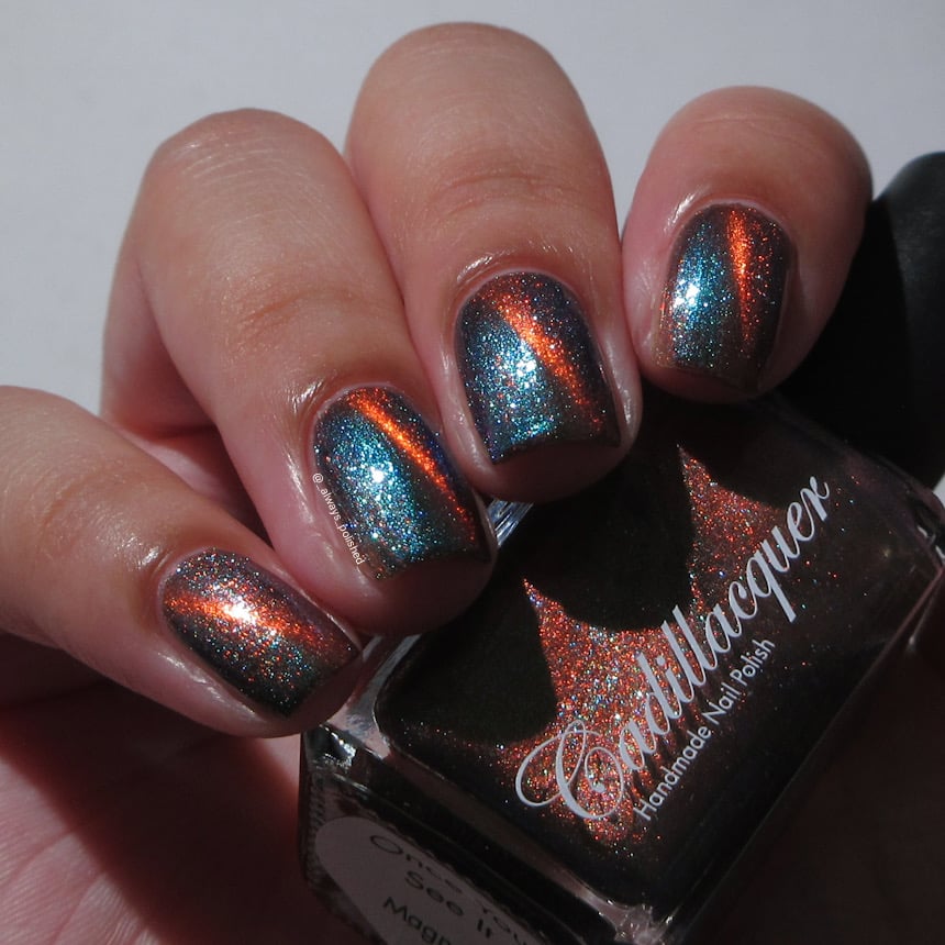 Magnetic multichrome shimmer Cadillacquer nail polish in Once You See It, swatched on five short natural nails showing a diagonal copper-orange magnetic band over a dark olive-brown base with shifting green-to-blue aurora shimmer, light skin tone, indoor warm lighting, swatched by @_always_polished_