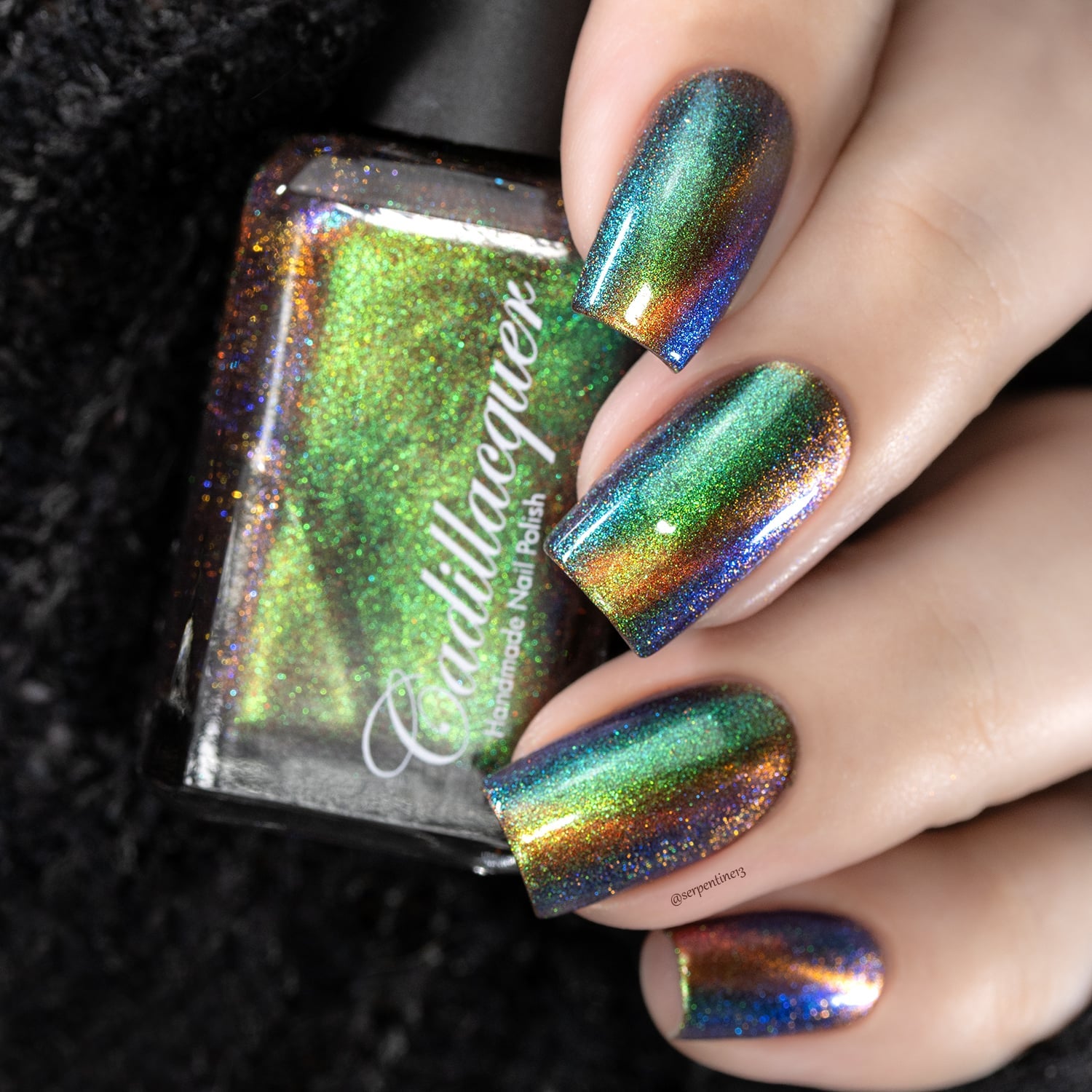 Holographic magnetic multichrome Cadillacquer nail polish in Once You See It, shown on four coffin-shaped nails beside the bottle, displaying a vivid lime-green to amber to electric blue colour-shifting aurora shimmer with a bright yellow-green magnetic cat-eye band over a deep steel-blue carrier base, light-medium skin tone, studio lighting, swatched by @serpentine13