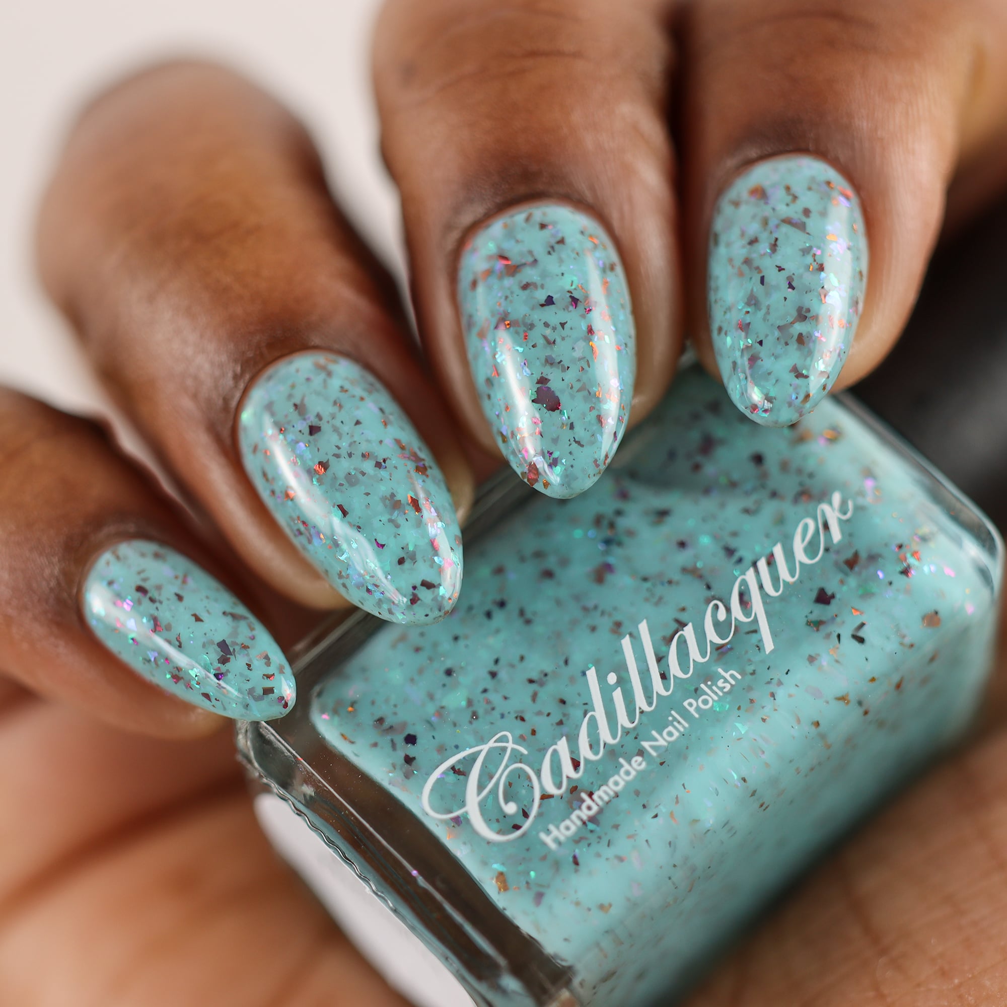 Cadillacquer Pastel Thoughts pastel teal purple chameleon iridescent crelly nail polish, bottle held with four-nail swatch, rich skin, studio lighting