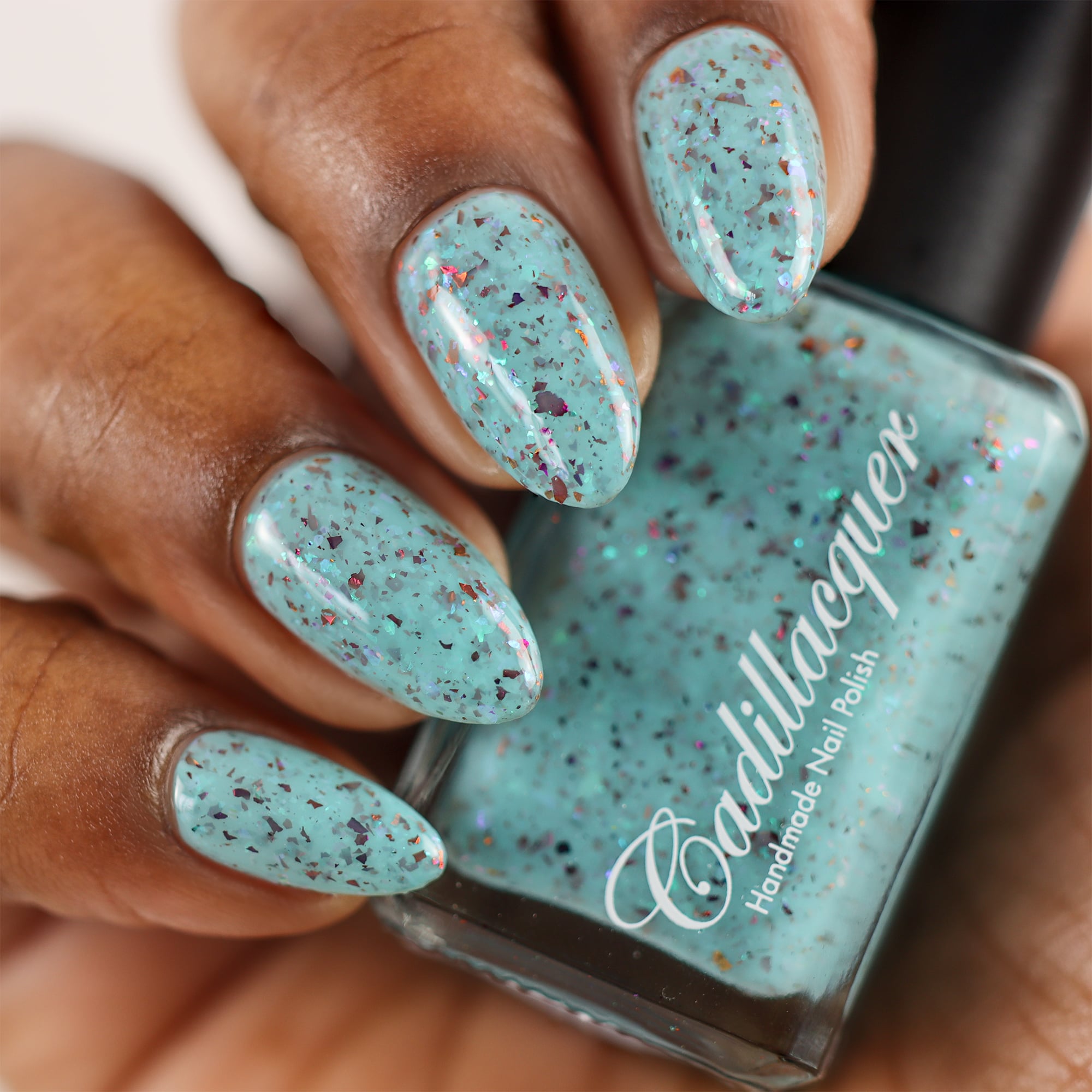 Cadillacquer Pastel Thoughts pastel teal purple chameleon iridescent crelly nail polish, bottle held with four-nail swatch, rich skin, studio lighting
