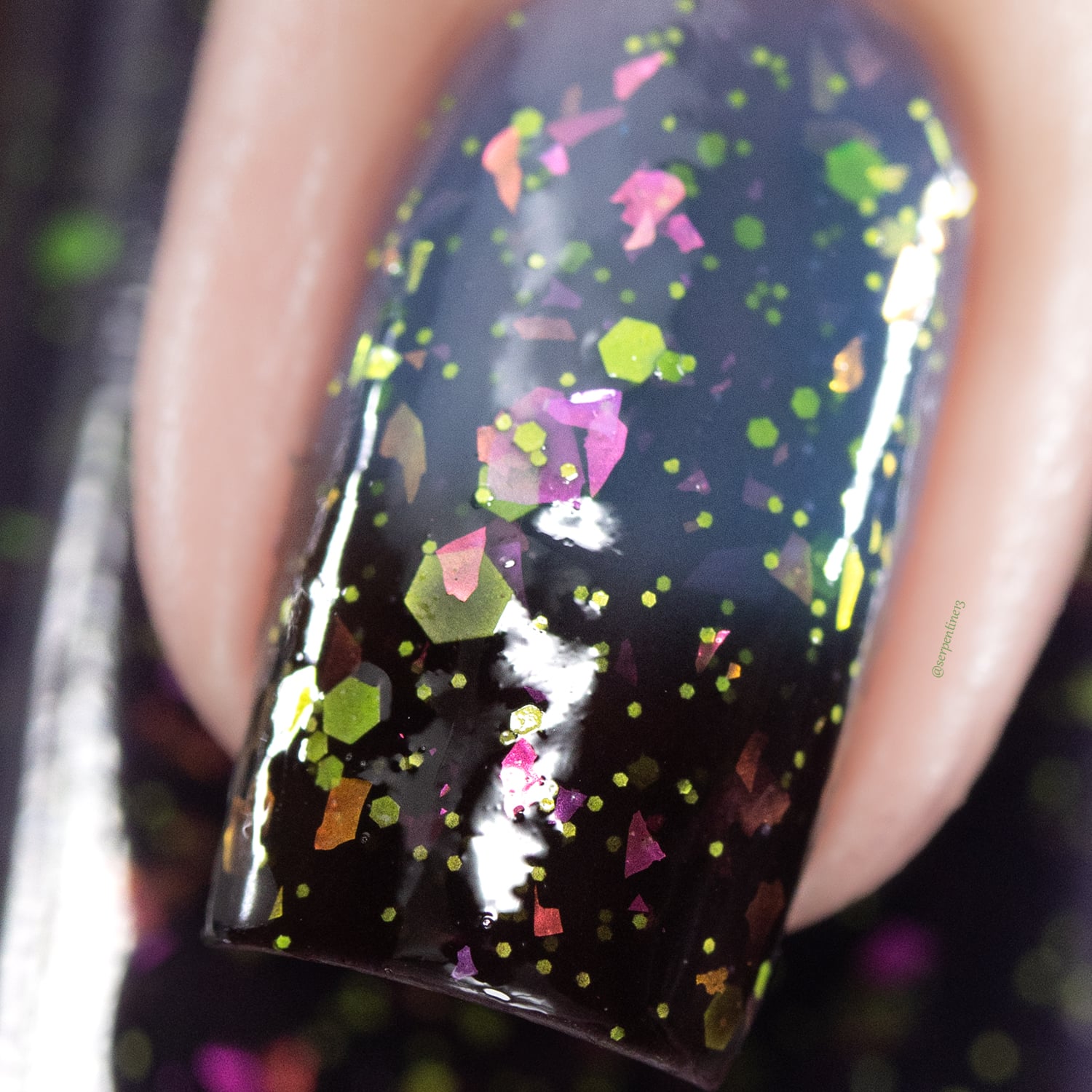 Thermal glitter-and-flake Cadillacquer nail polish in Strange Happenings, extreme macro closeup of a single square nail in the cold state showing a near-black blackened eggplant base densely packed with neon yellow-green matte hexagonal glitter in multiple sizes and large iridescent pink, magenta, violet, and orange flakes, light skin tone, studio lighting, swatched by @serpentine13