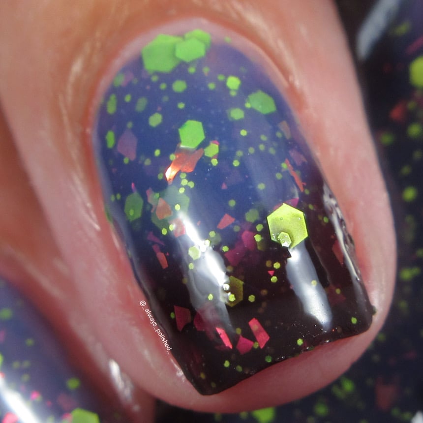 Thermal glitter and iridescent-flake nail polish swatch of Cadillacquer Strange Happenings, showing a transition from near-black blackened eggplant at the nail tips to dusty blue at the base, densely packed with matte neon green hexagon and dot glitter in multiple sizes and pink-to-orange iridescent flakes, on light-medium skin in bright daylight, swatched by @_always_polished_