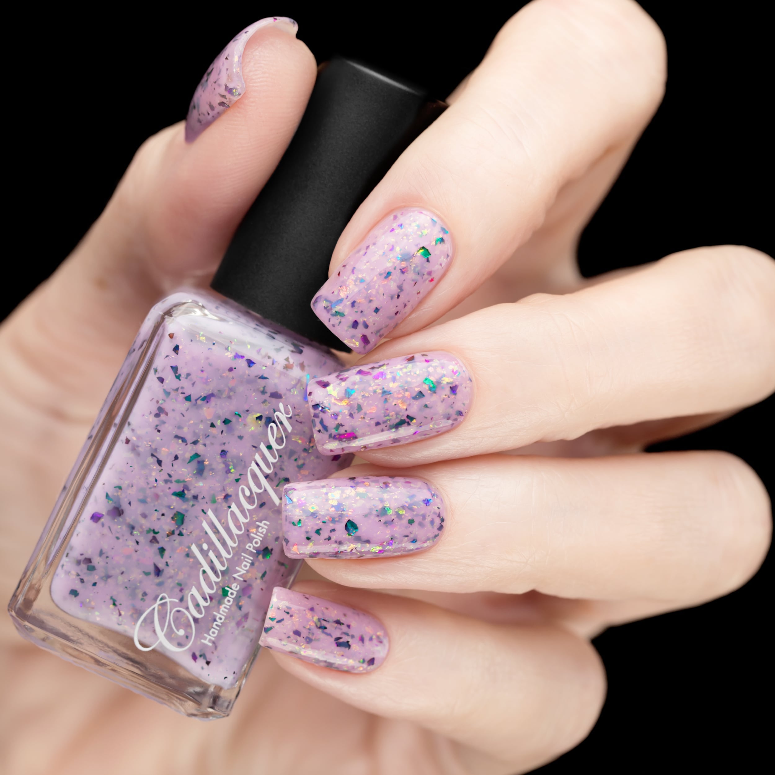 Cadillacquer Sweet Nothing pink teal chameleon iridescent crelly nail polish, bottle held with five-nail swatch, light skin, studio lighting