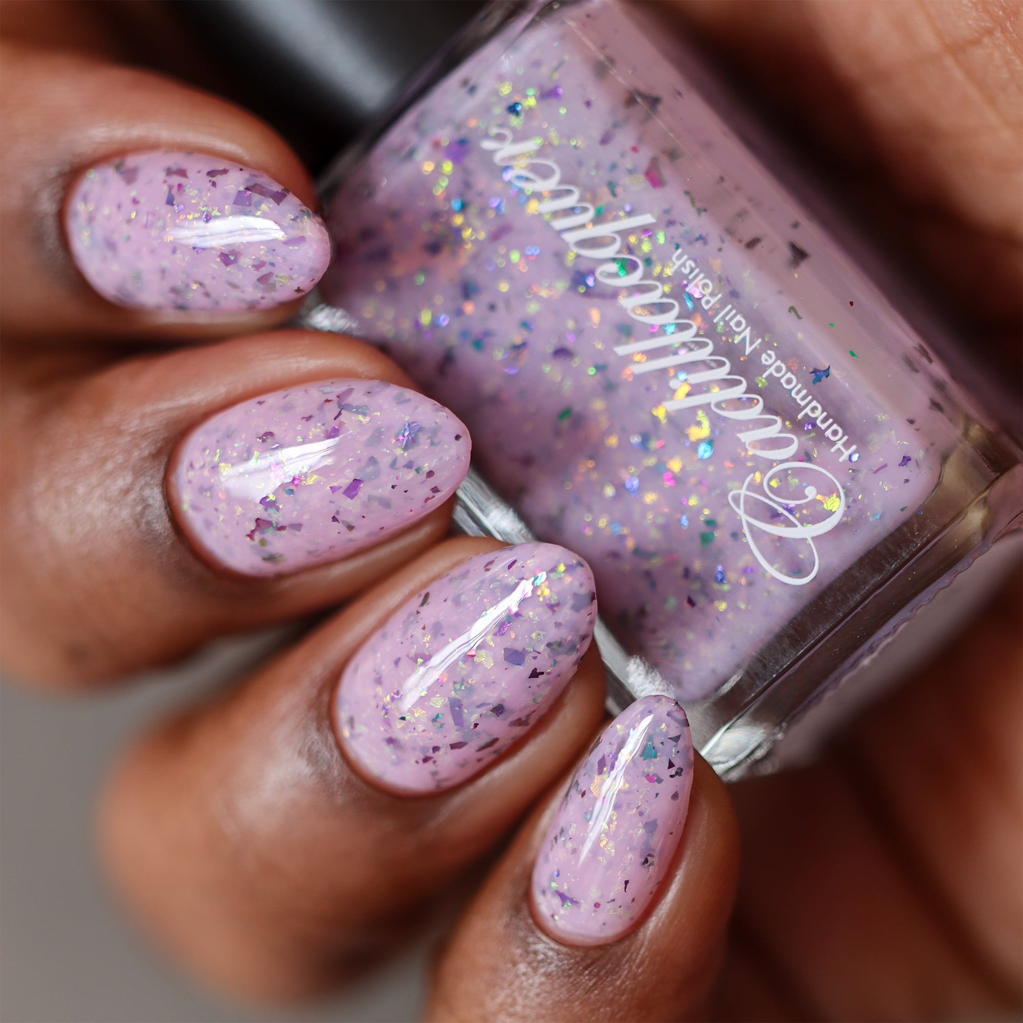 Cadillacquer Sweet Nothing pink teal chameleon iridescent crelly nail polish, bottle held with four-nail swatch, deep skin, studio lighting