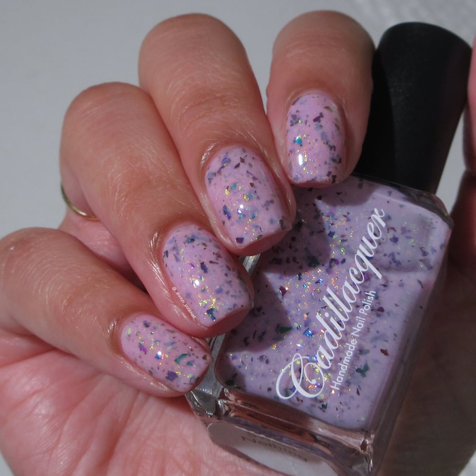 Cadillacquer Sweet Nothing pink teal chameleon iridescent crelly nail polish, bottle held with four-nail swatch, light skin, indoor warm lighting