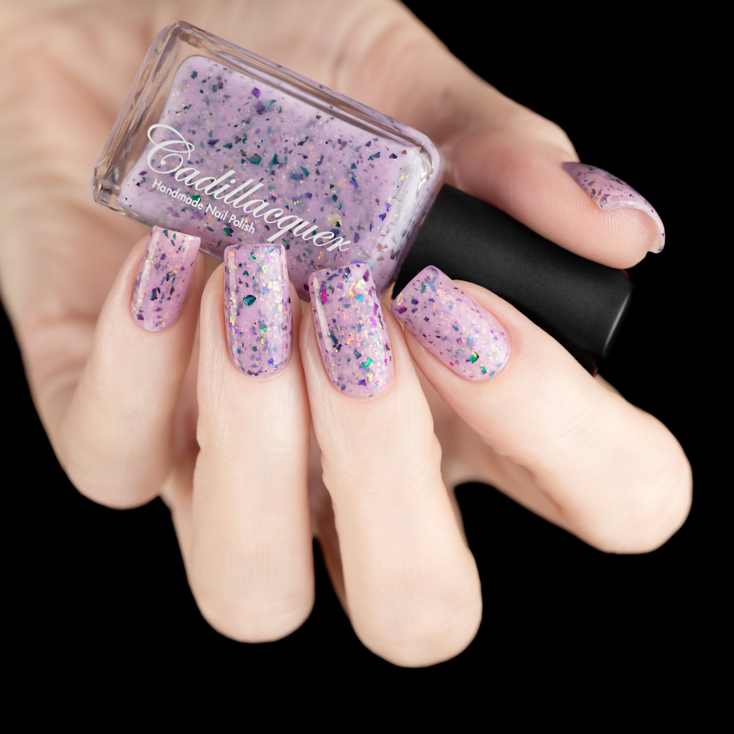 Cadillacquer Sweet Nothing pink teal chameleon iridescent crelly nail polish, bottle held with five-nail swatch, light skin, studio lighting