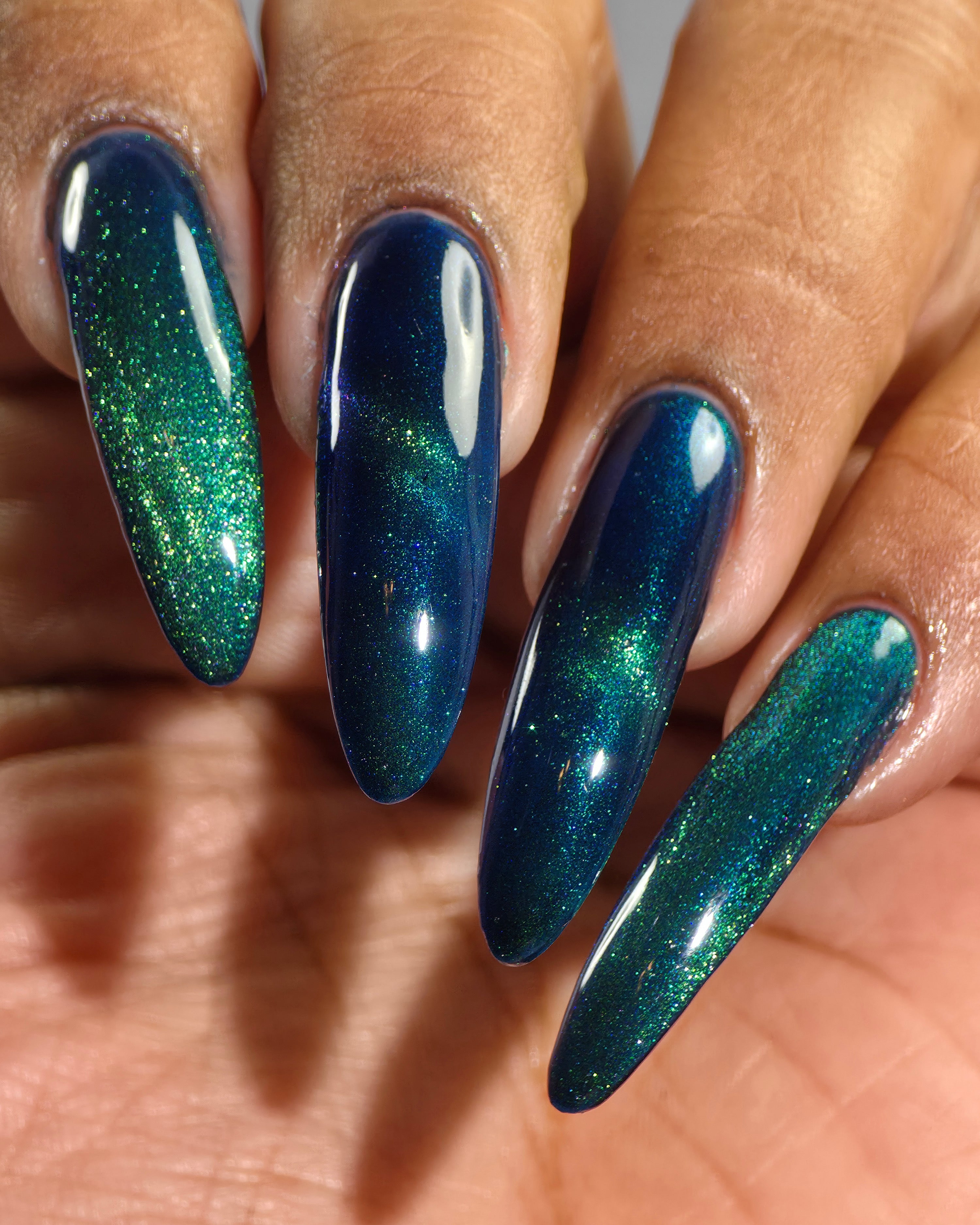 Do-Nuts by Glitch Lacquer, deep blue jelly, green-to-teal-to-blue magnetic, on medium-deep skin tone stiletto nails