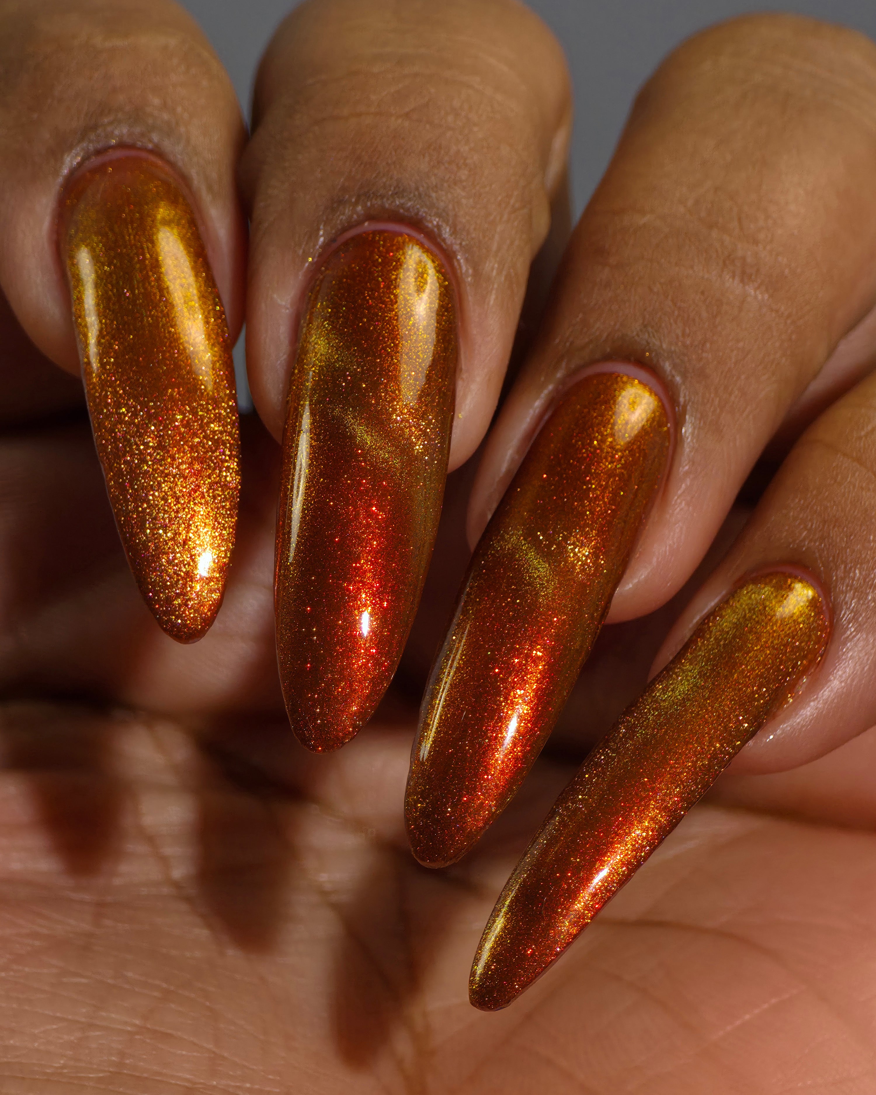 Marigold by Glitch Lacquer, burnt orange jelly, red shimmer, orange-to-gold magnetic, on medium-deep skin tone stiletto nails