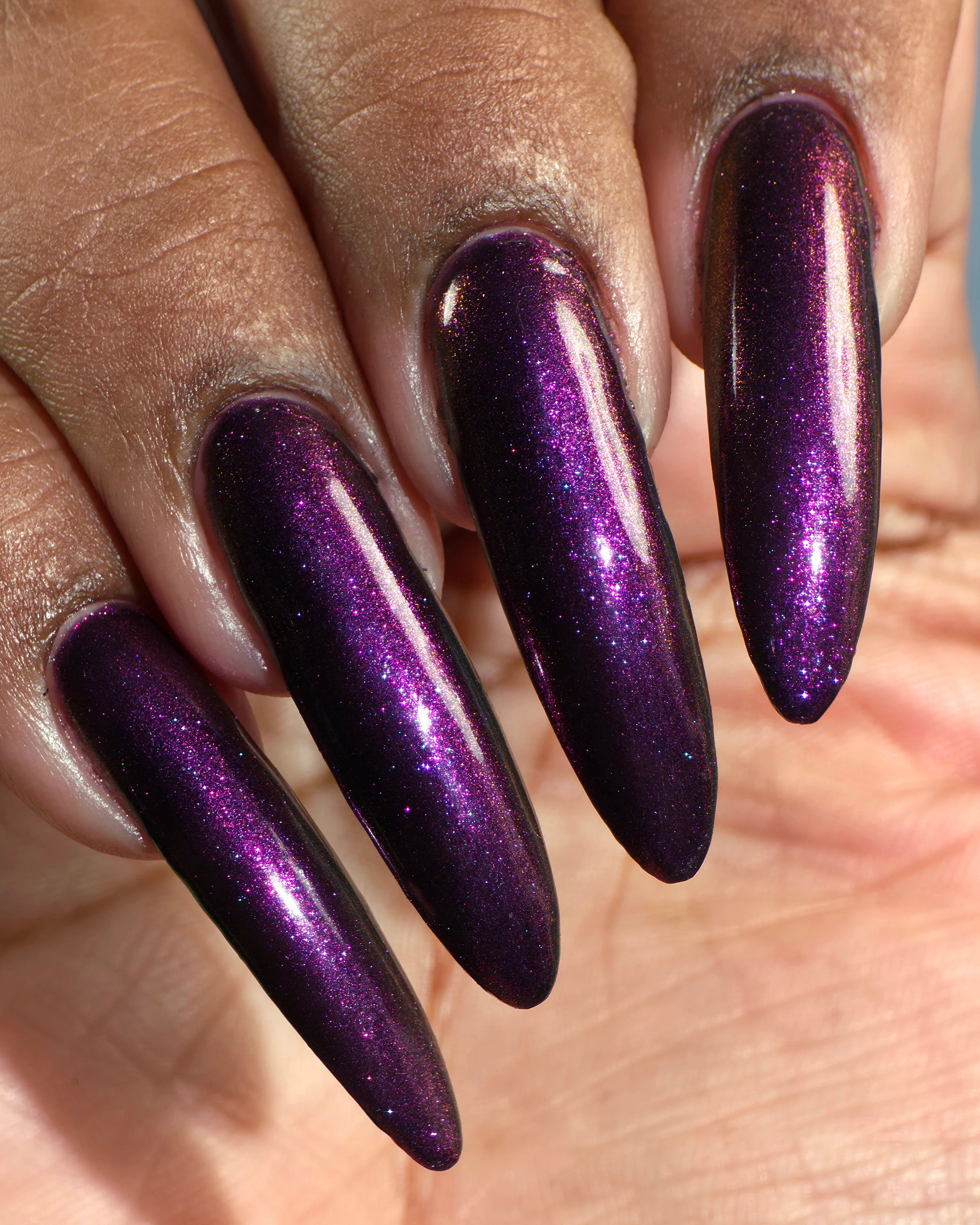 Sister Outsider by Glitch Lacquer, blackened purple jelly with magenta-purple sparkle, on deep skin tone stiletto nails