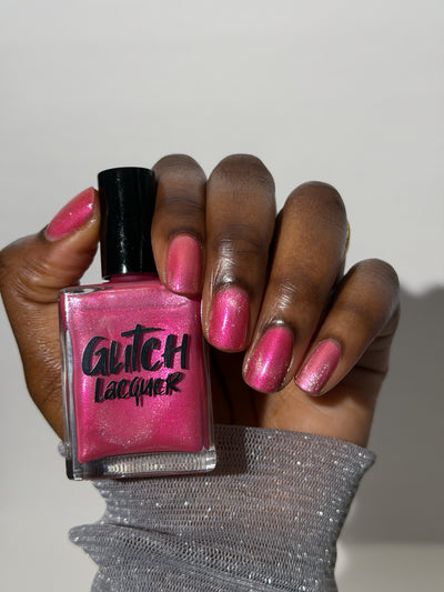 Lovey Dovey by Glitch Lacquer bottle held in hand with five round-to-squoval nails swatched, warm pink polish with pink-to-gold reflective shimmer and silver magnetic pigment, deep skin tone, studio lighting.