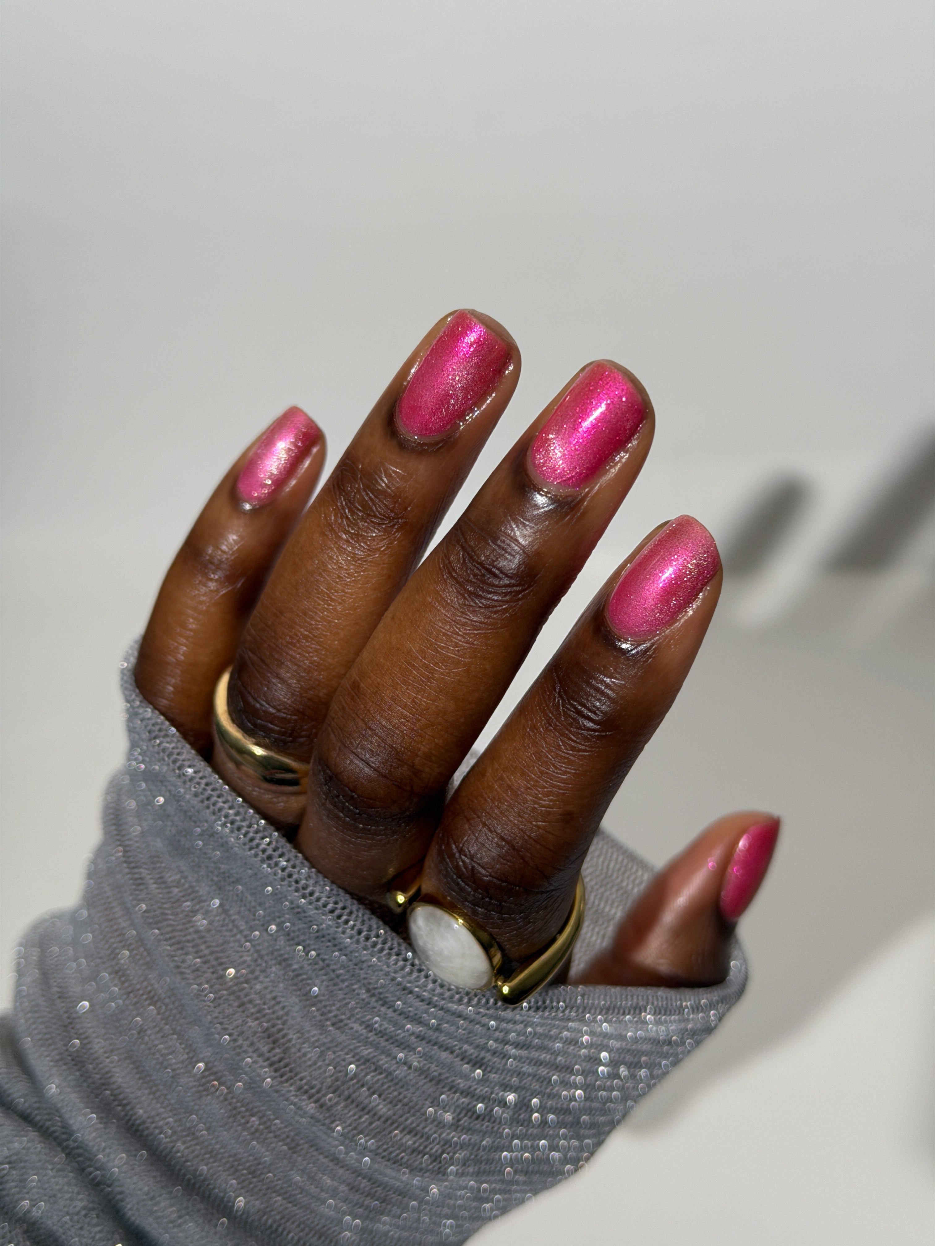 Lovey Dovey by Glitch Lacquer on five round nails, warm pink polish with pink-to-gold reflective shimmer and silver magnetic pigment, deep skin tone, bright studio lighting.