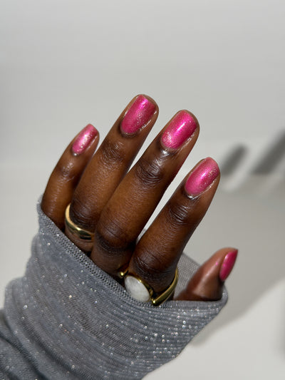 Lovey Dovey by Glitch Lacquer on five round nails, warm pink polish with pink-to-gold reflective shimmer and silver magnetic pigment, deep skin tone, bright studio lighting.