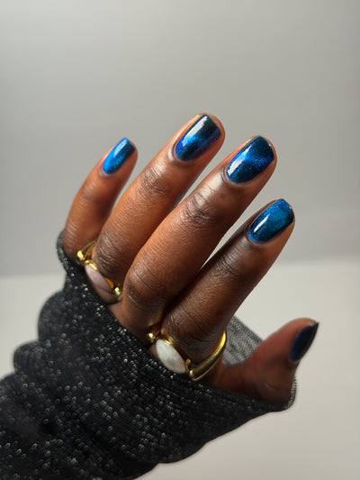 Heart of the Ocean by Glitch Lacquer swatched on five squoval nails, deep blue magnetic jelly with blue glitters, deep skin tone, studio lighting.
