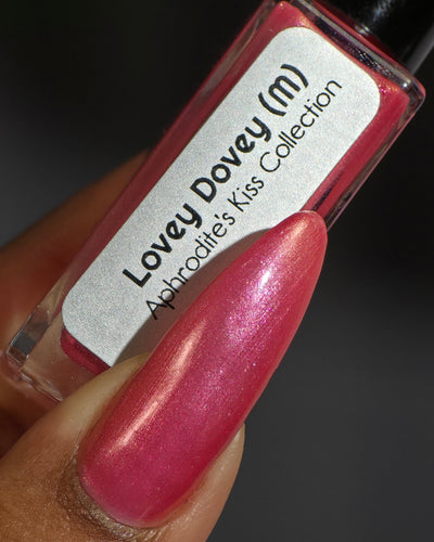 Lovey Dovey by Glitch Lacquer bottle held in hand with one long almond nail swatched, warm pink polish with pink-to-gold reflective shimmer and silver magnetic pigment, deep skin tone, studio lighting.