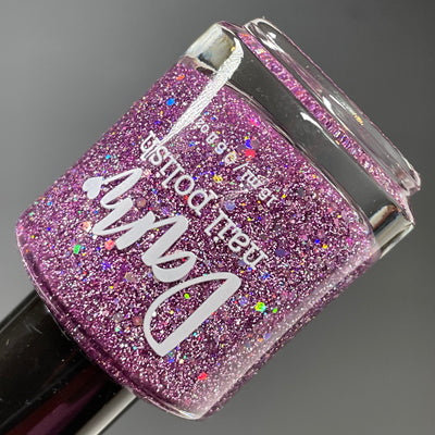 Thistle be the Day by Dam Nail Polish, warm purple jelly with silver holo micro-glitter and iridescent hex glitter pieces under studio light, bottle standalone product shot